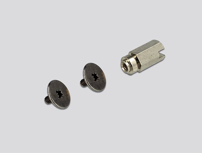 Vis métalliques à têtes plates et pièce cylindrique métallique filetée à l'intérieur, disposées sur un fond gris.