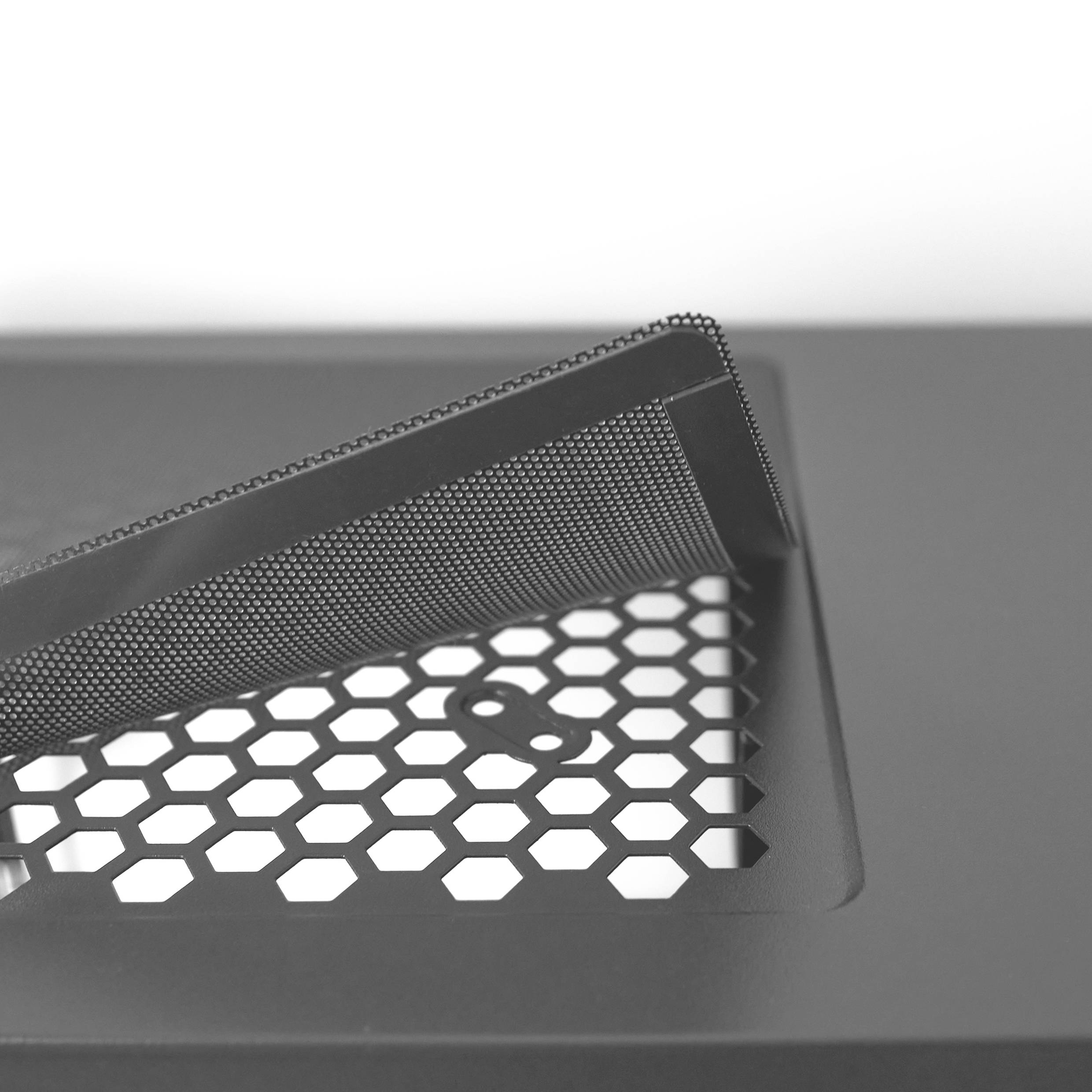 Une photo en noir et blanc montre un tamis à grille hexagonal ouvert posé sur une surface lisse, probablement une grille de ventilation.