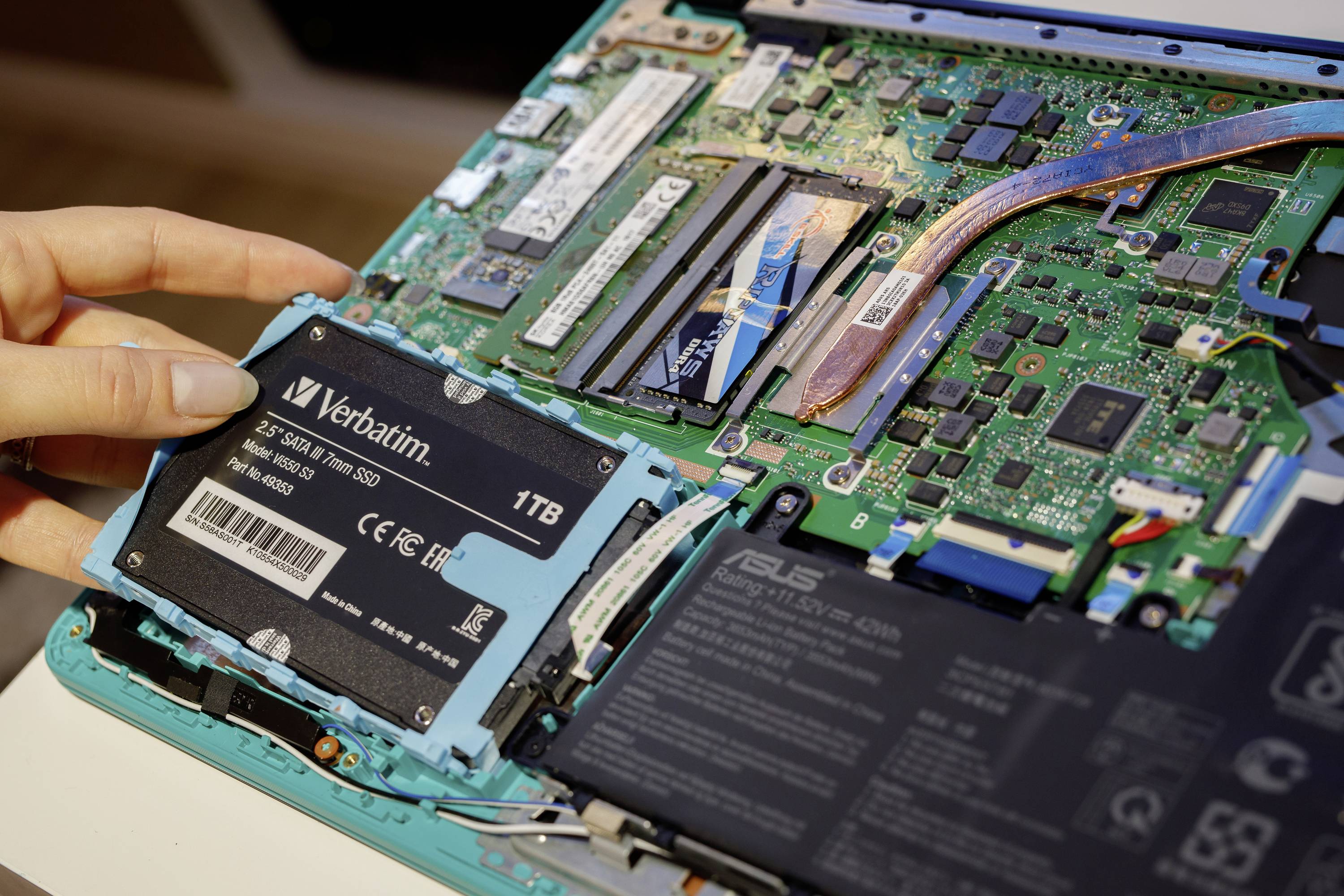 Une main installe un disque SSD de 1 To dans un ordinateur portable ouvert avec des composants électroniques et des circuits apparents.