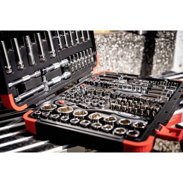 Une boîte à outils ouverte remplie de diverses clés à douille métalliques et d'outils, rangés dans un étui noir et rouge, posée sur une surface texturée.