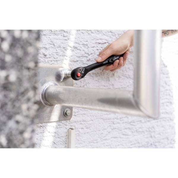 Une personne utilise une clé à molette noire pour serrer un boulon sur un garde-corps métallique fixé à un mur texturé.