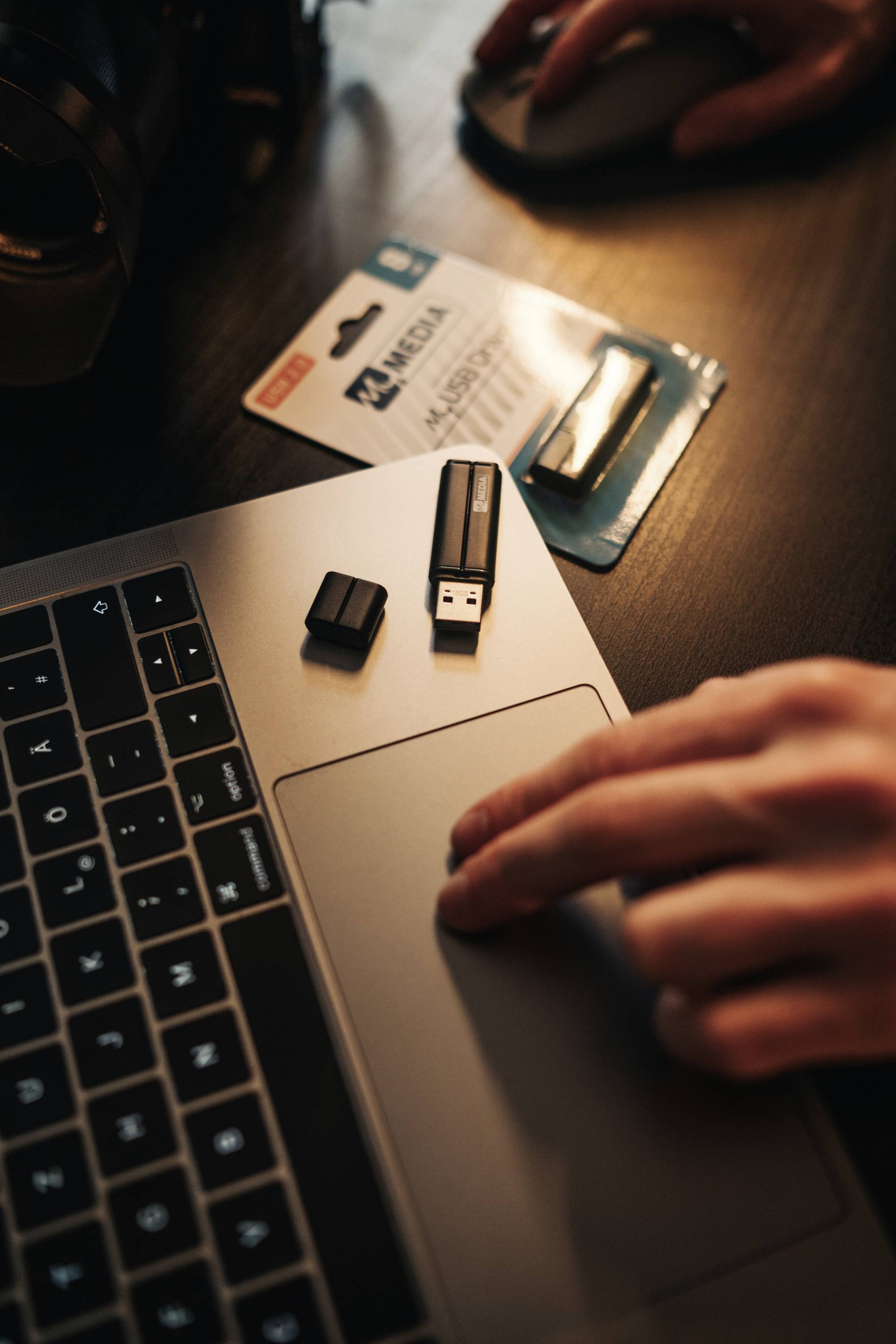 Une main sur un pavé tactile d'ordinateur portable, à côté une clé USB et un emballage contenant une autre clé USB.