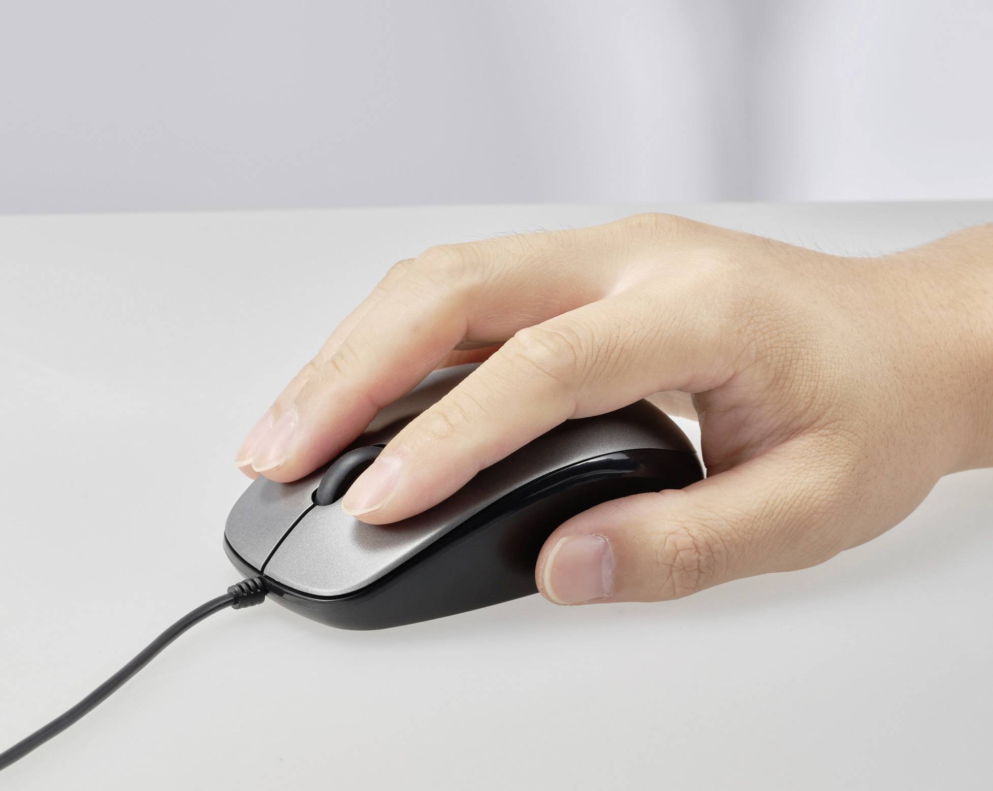 Une main tient et manipule une souris d'ordinateur filaire sur une table.