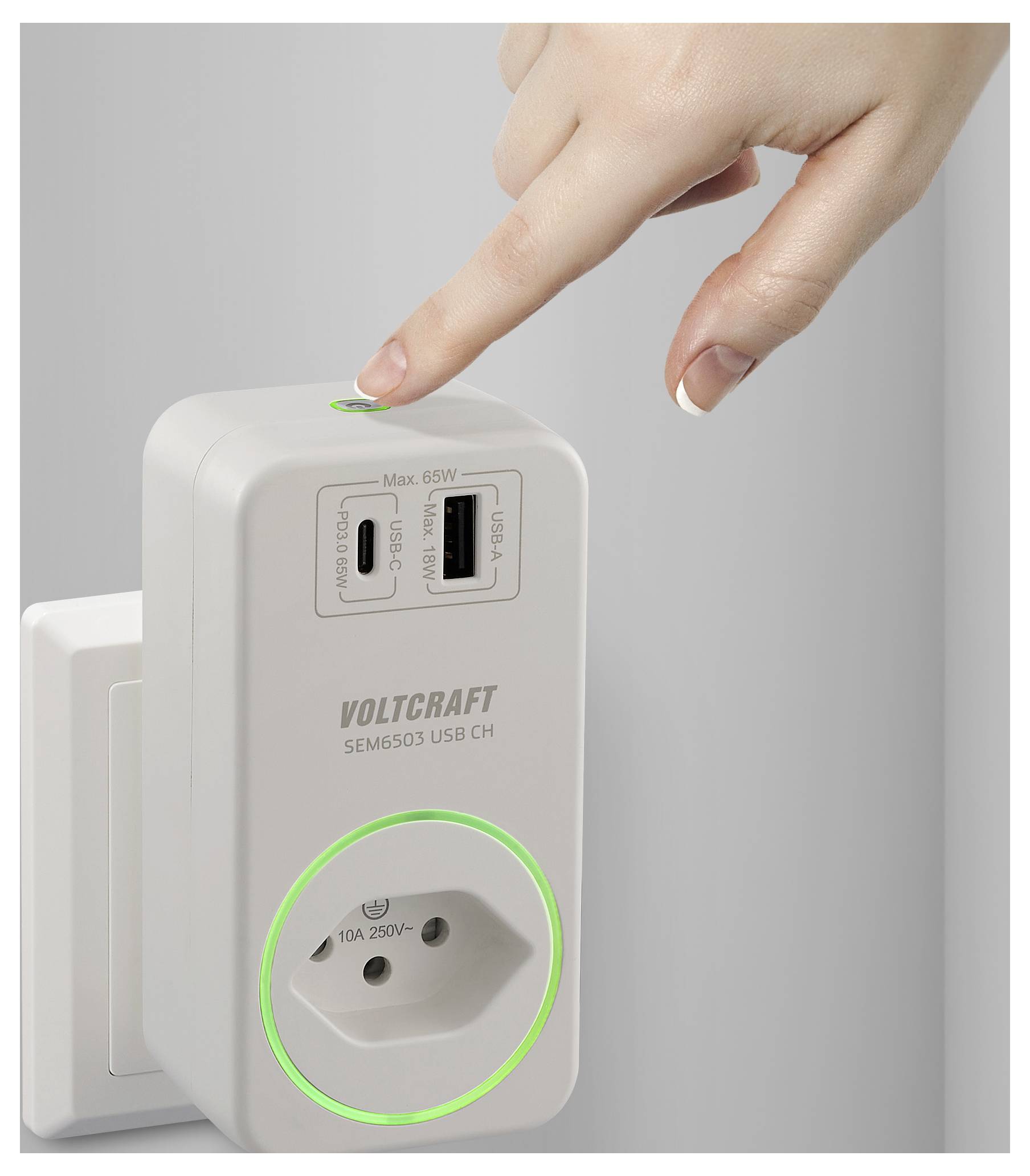 Une main appuyant sur un bouton d'un chargeur USB Voltcraft branché dans une prise électrique, avec deux ports USB et une prise de courant.