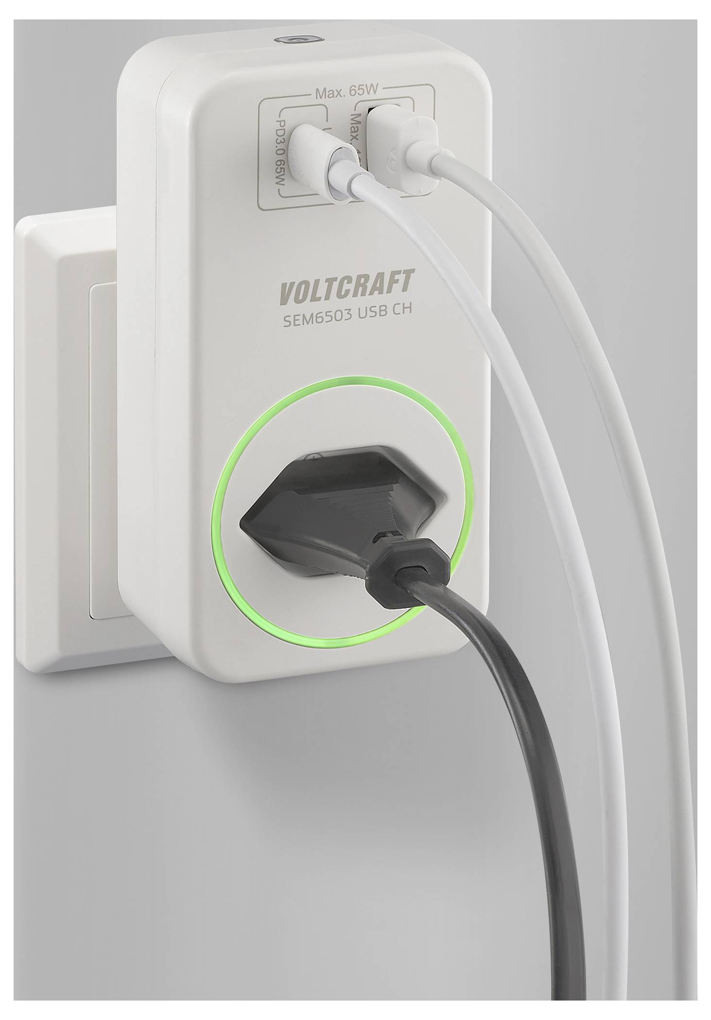 Un compteur de puissance Voltcraft blanc branché dans un mur, affichant deux câbles USB et un câble d'alimentation connectés, avec un anneau lumineux vert.