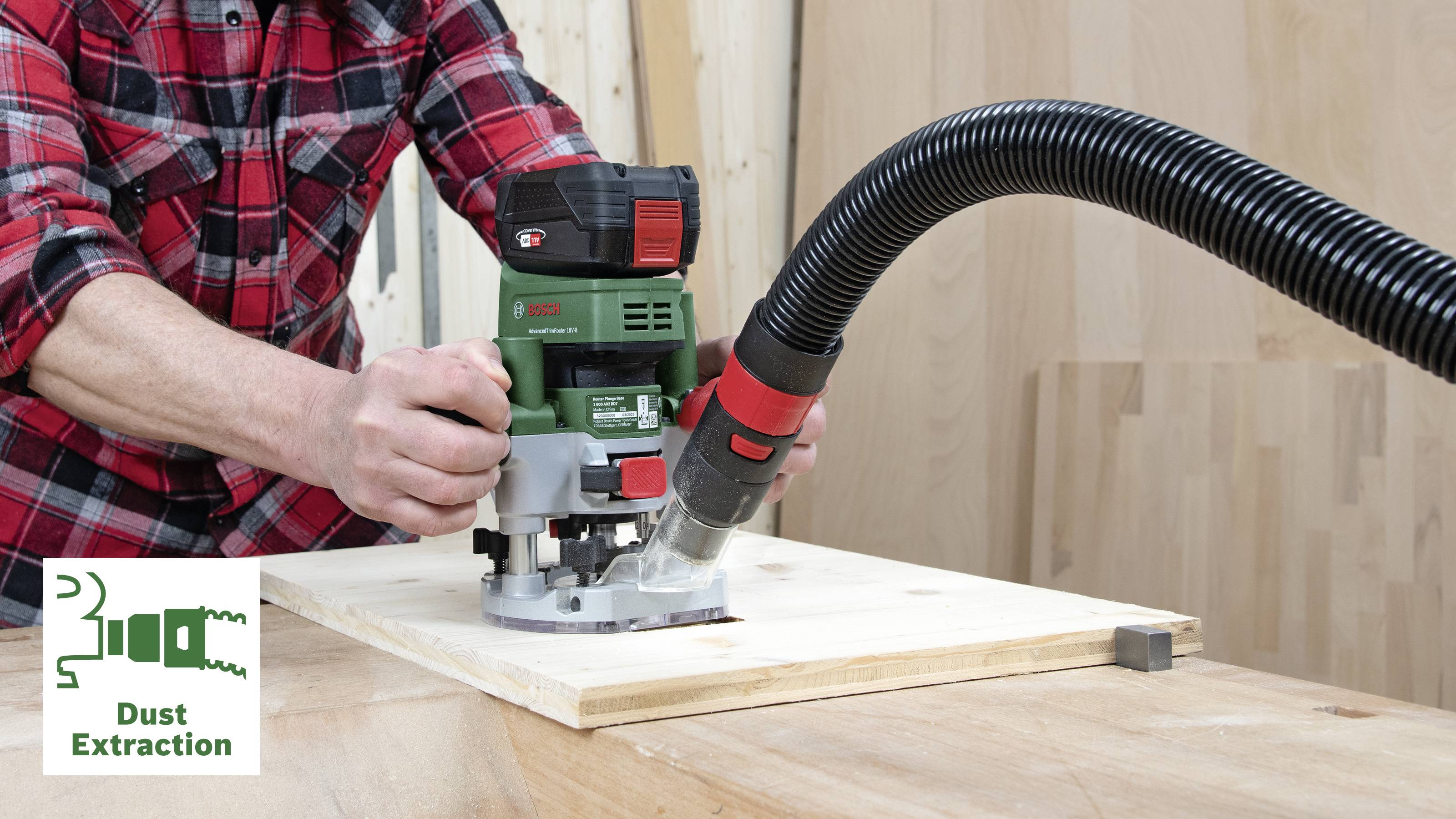 Une personne utilise une défonceuse verte sur une planche en bois. Un tuyau d'aspiration est raccordé à l'appareil.
