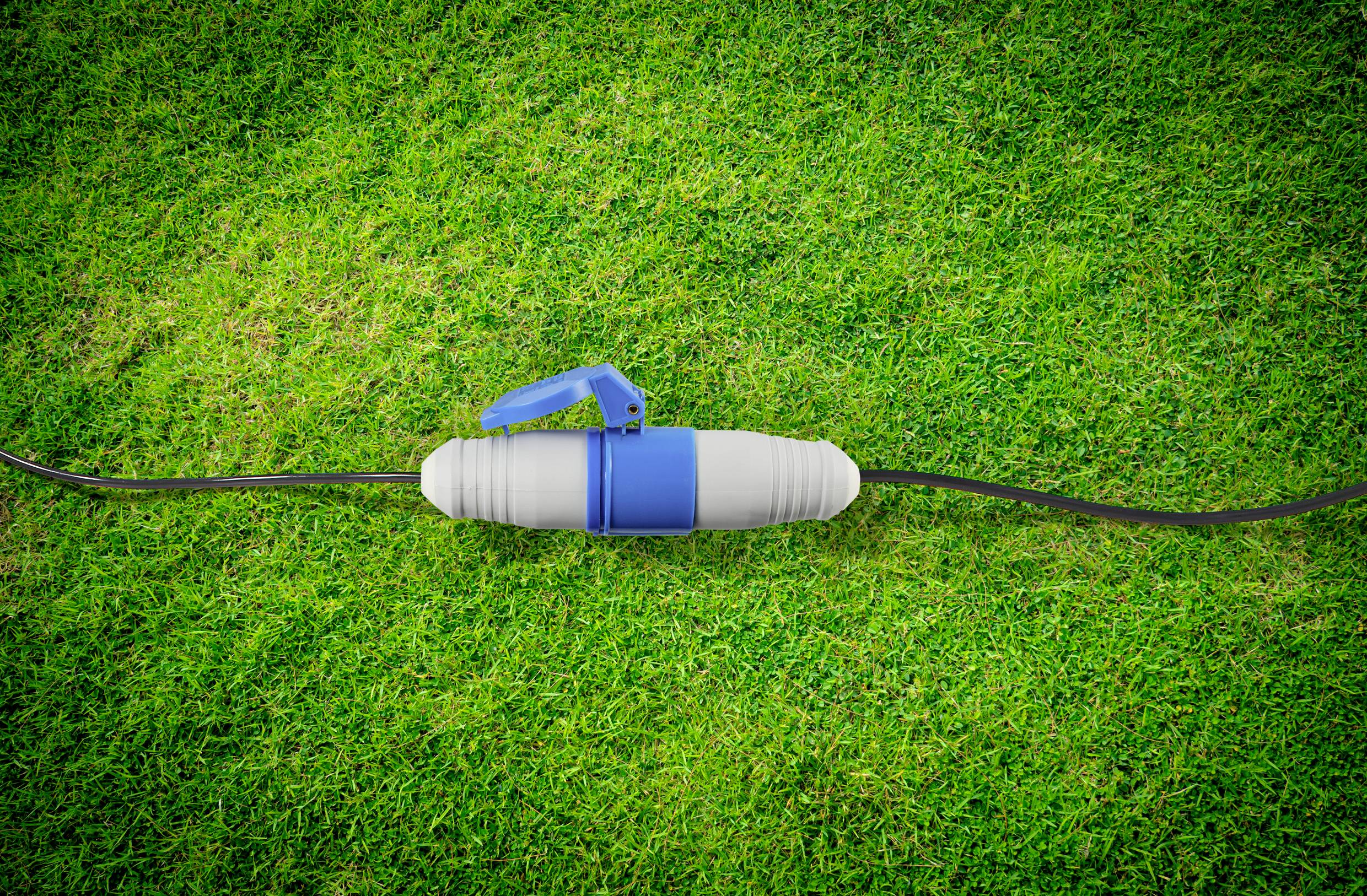 Une poignée bleue sur un long tuyau noir repose sur de l'herbe verte. La poignée est fixée à un cylindre gris.
