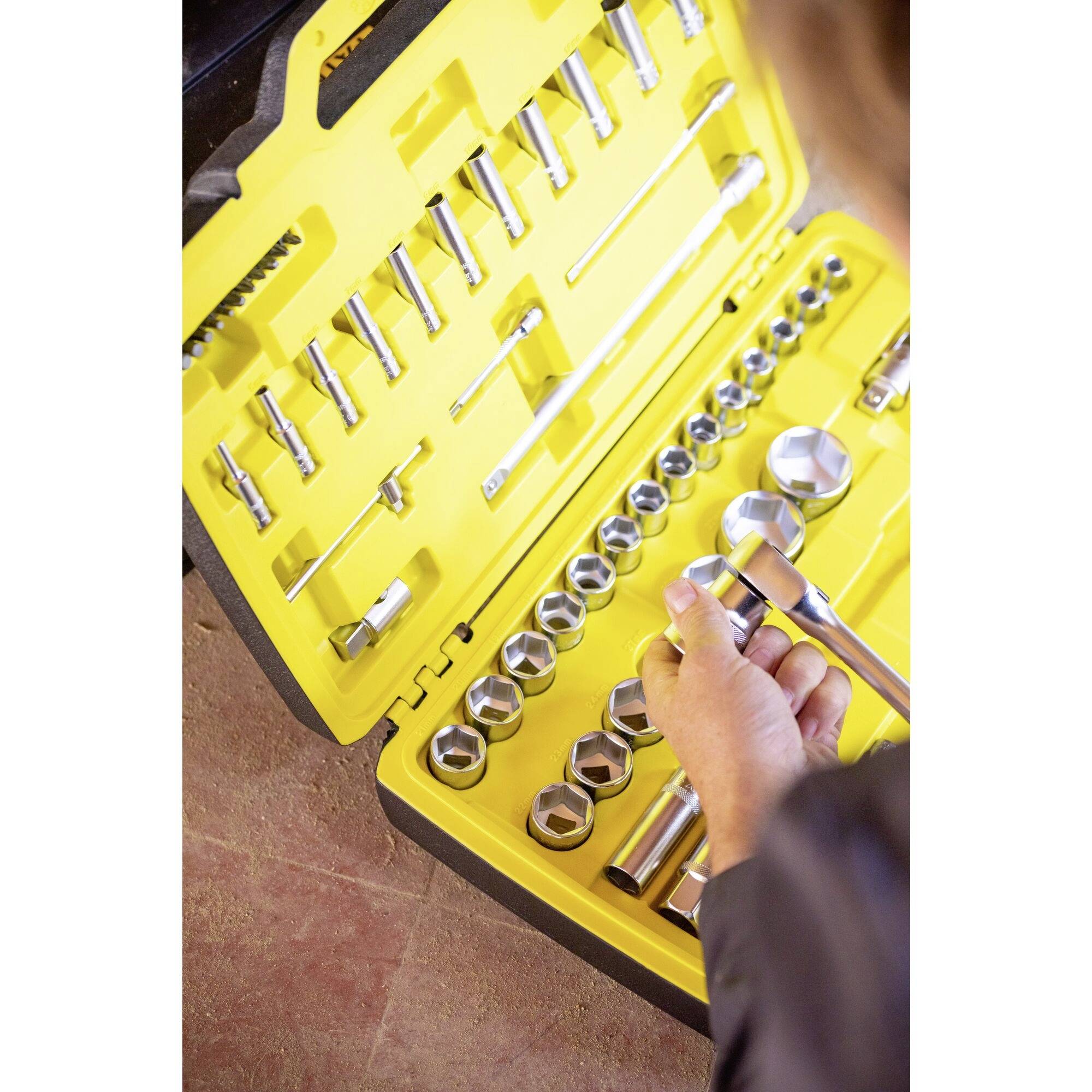 Une mallette à outils ouverte avec un intérieur jaune présente une sélection de clés à cliquet. Une main choisit l'une des clés.