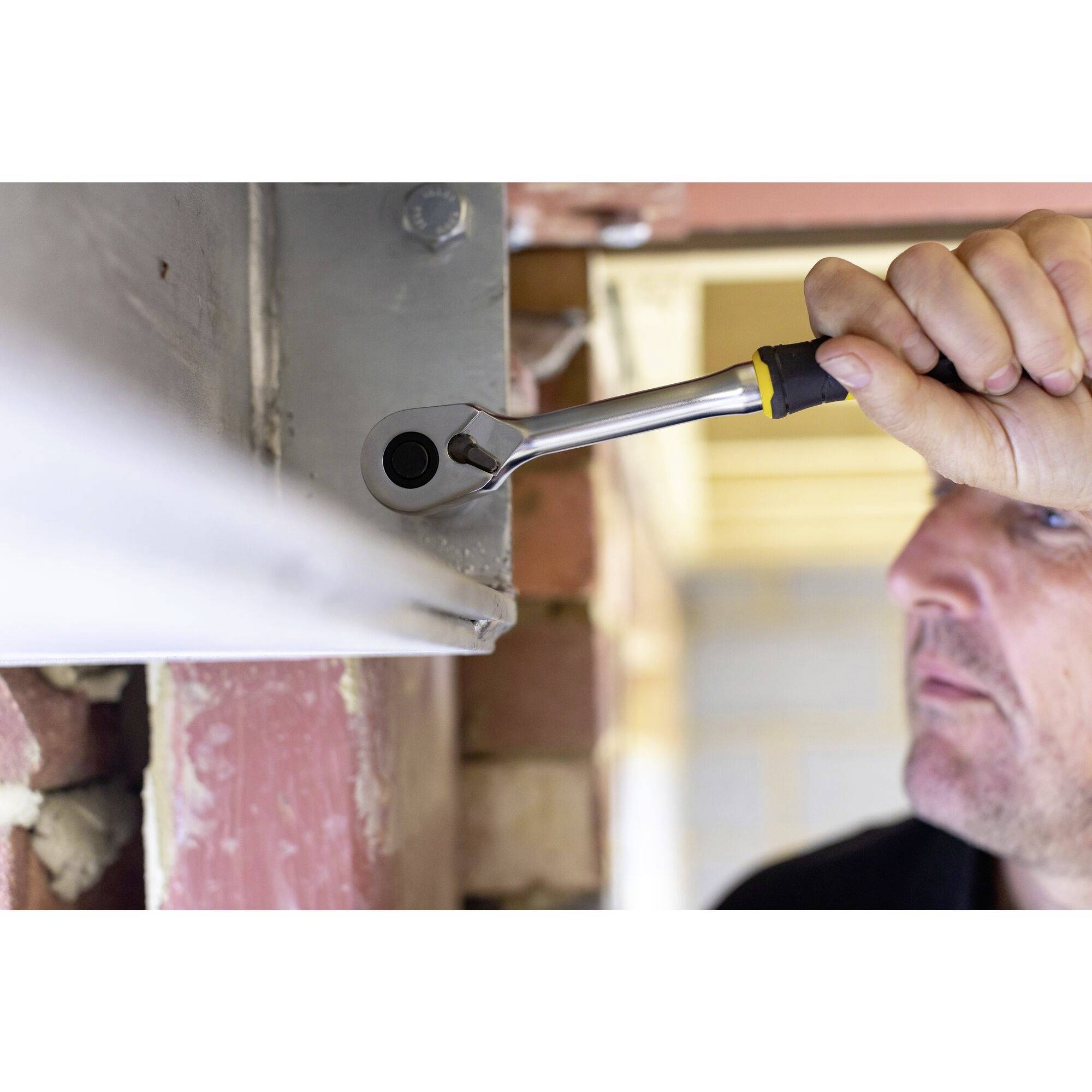Une personne visse une vis avec une clé à molette dans une poutre métallique afin de créer une construction stable. En arrière-plan, des murs non enduits sont visibles.