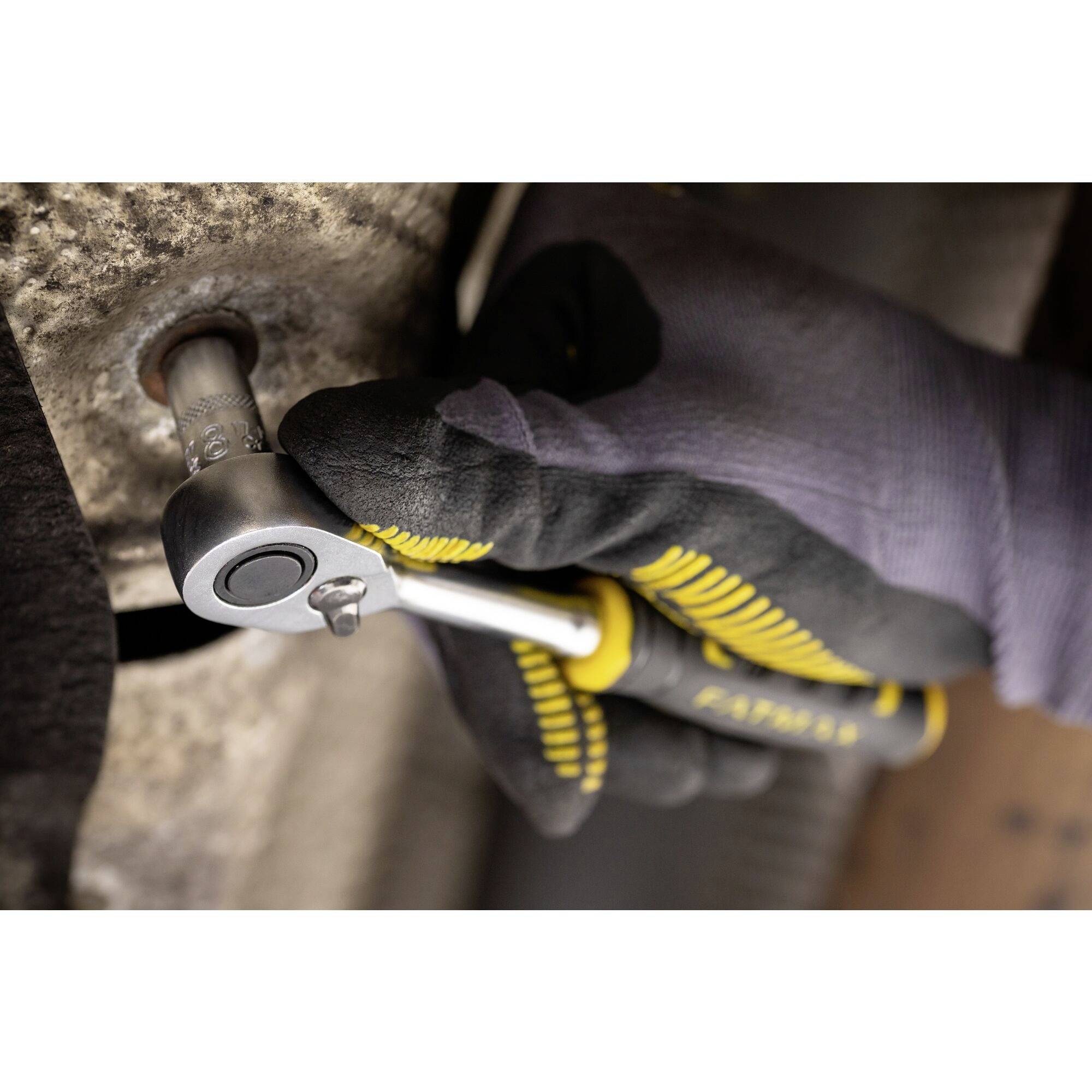 Une personne portant des gants noirs et jaunes serre une vis à l'aide d'un outil à cliquet.