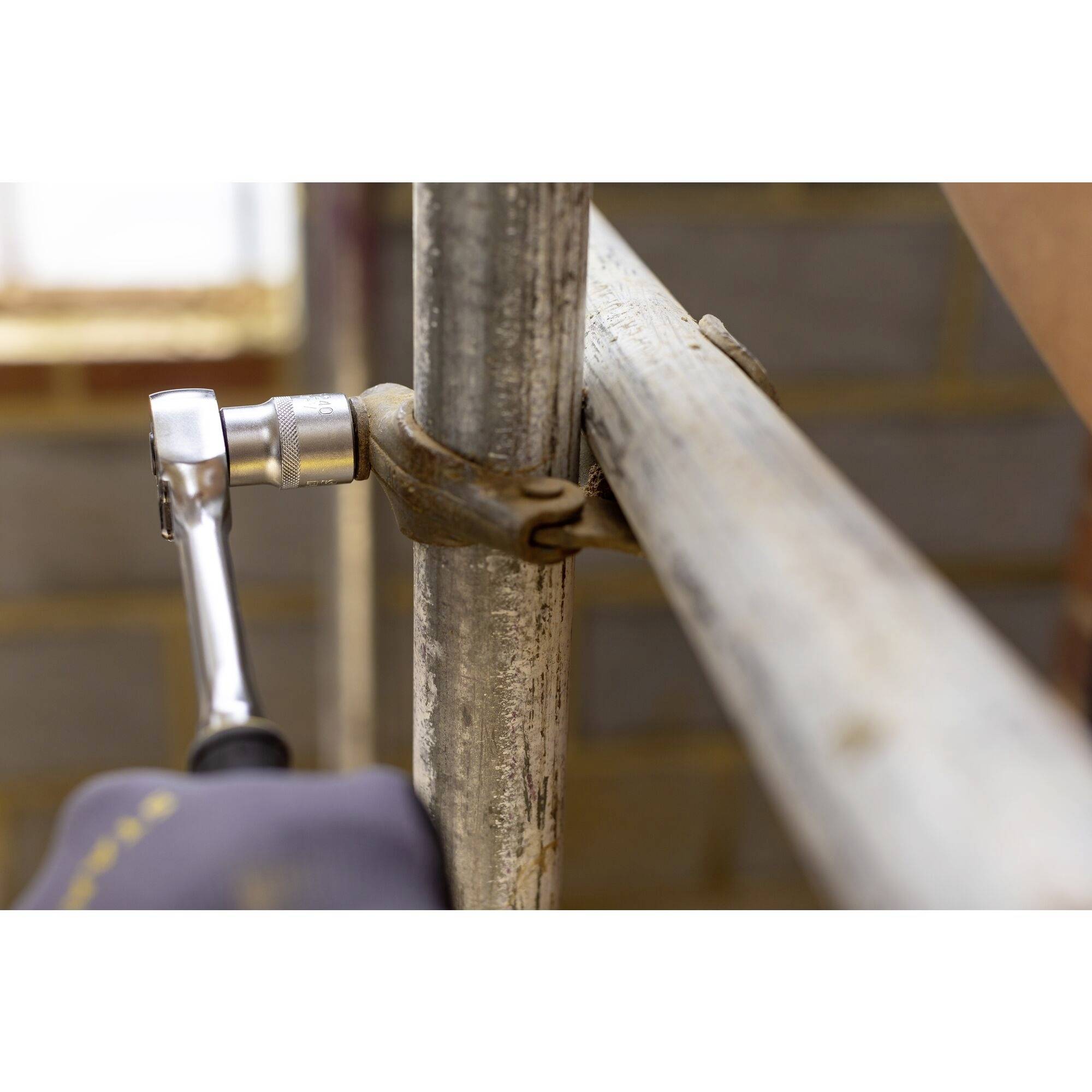 Un homme utilise une clé à cliquet pour fixer une connexion métallique dans une structure d'échafaudage ; illustre le processus de fixation.