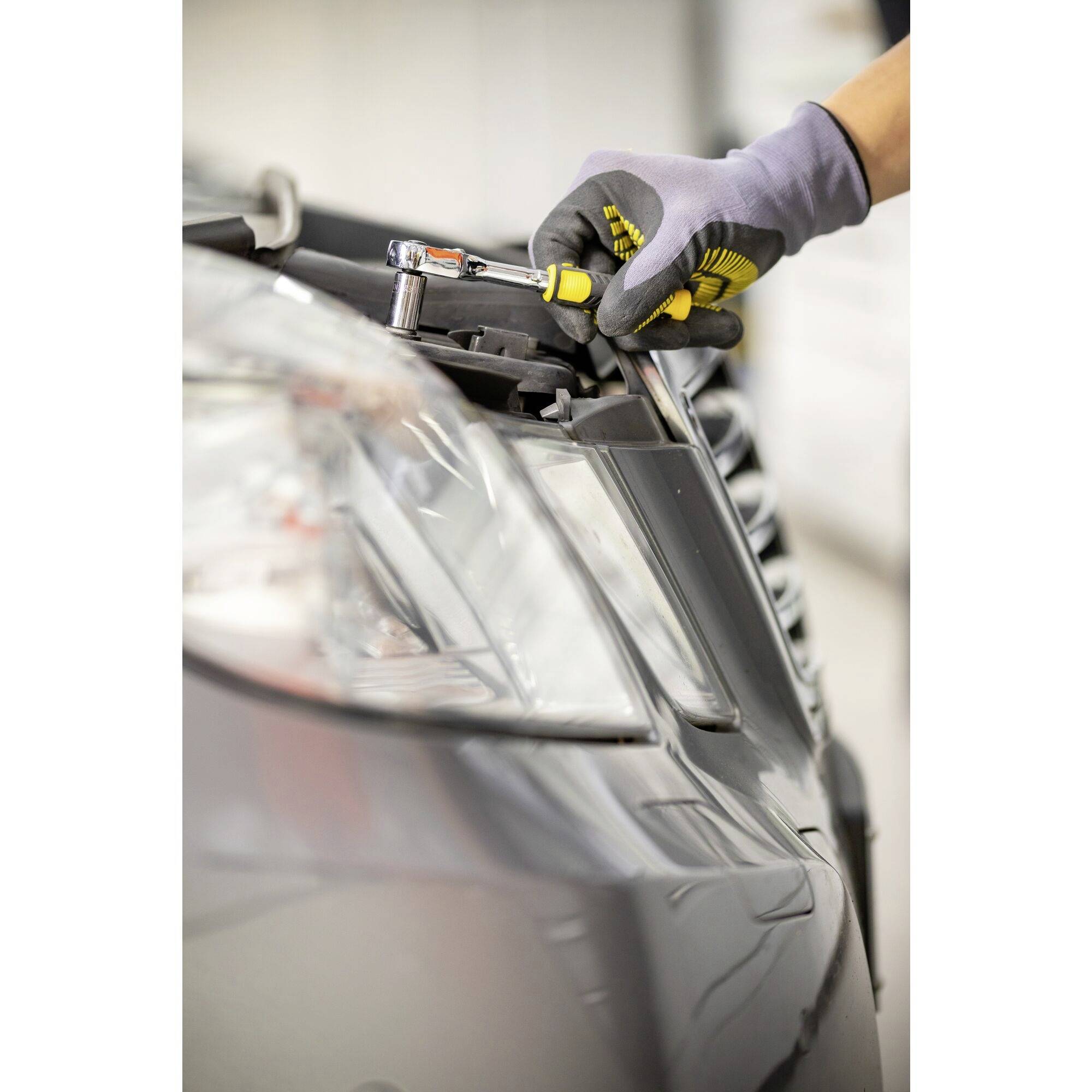 Une personne répare un phare de voiture avec des gants et des outils.