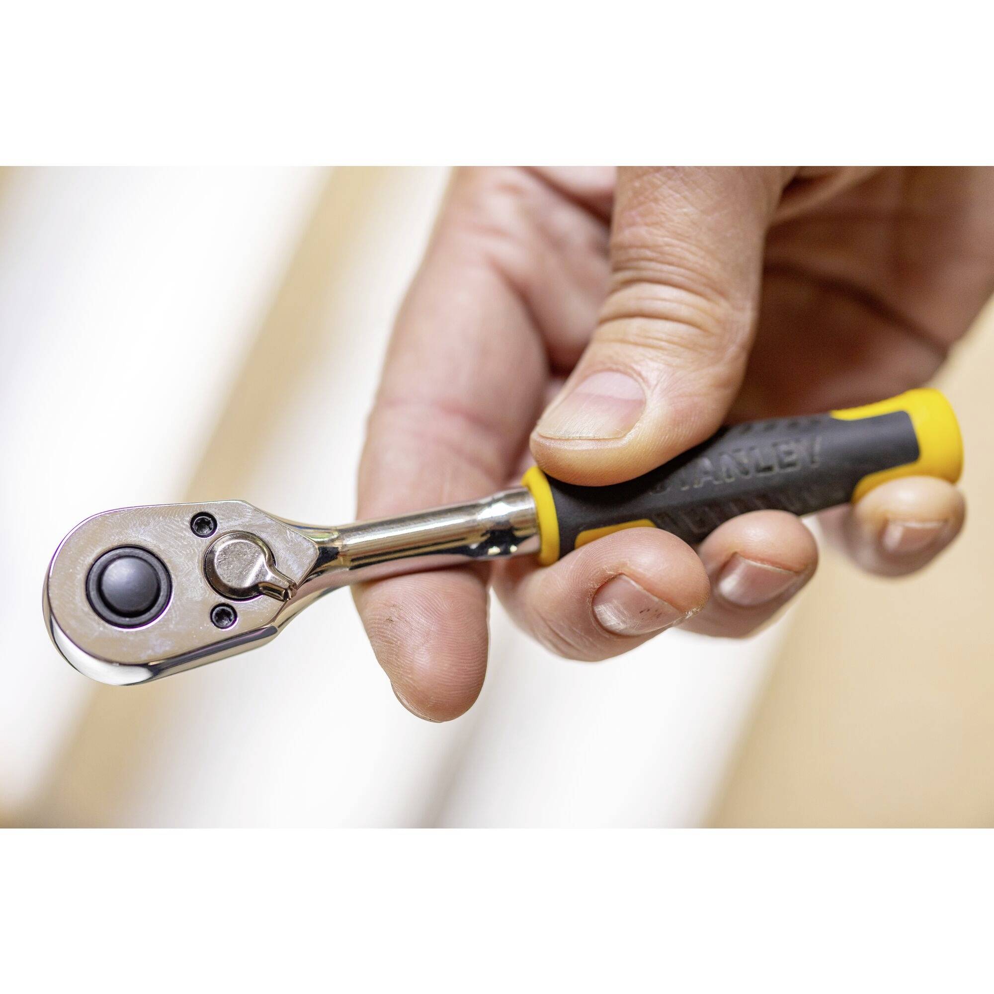 Une main tient une petite clé à cliquet avec une poignée jaune et noire, adaptée à une utilisation en mécanique.