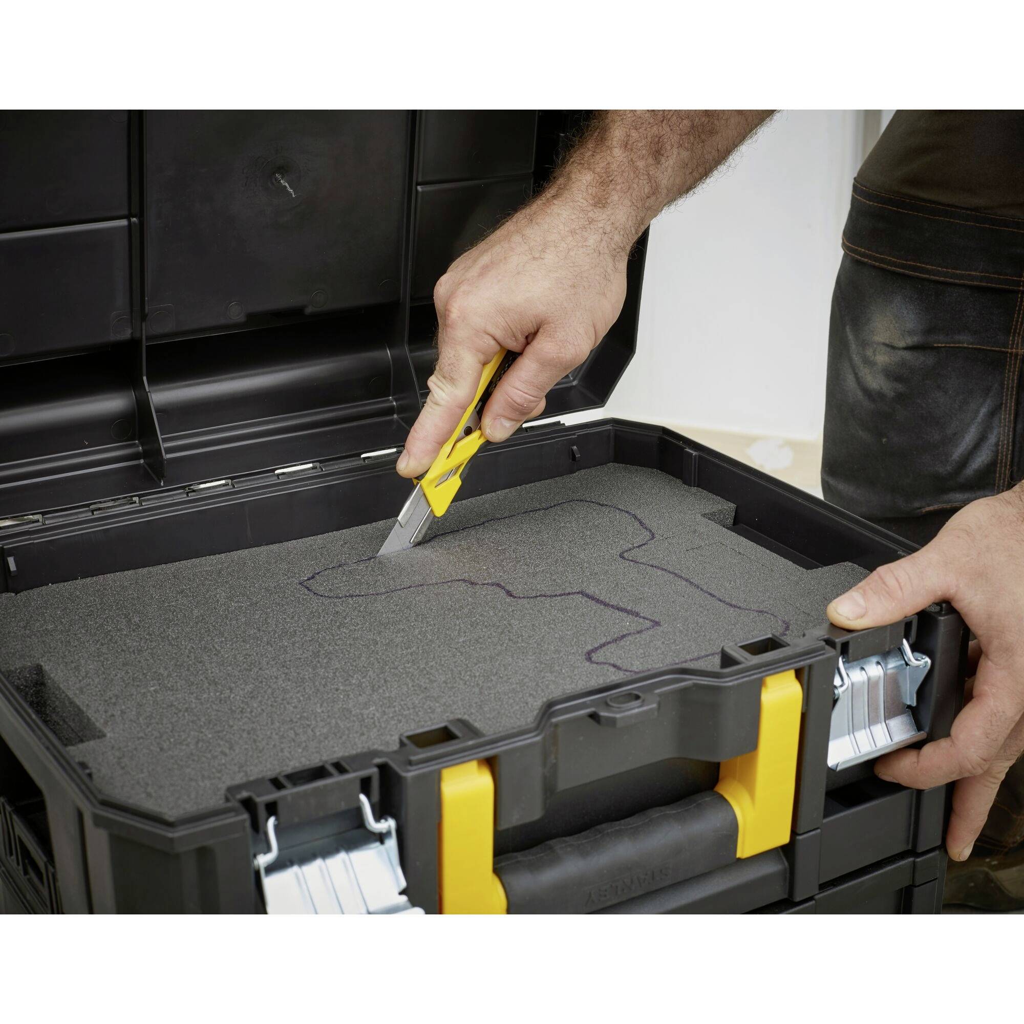 Une personne découpe de la mousse avec un couteau utilitaire dans une boîte à outils. La mousse comporte des marquages pour une coupe précise.