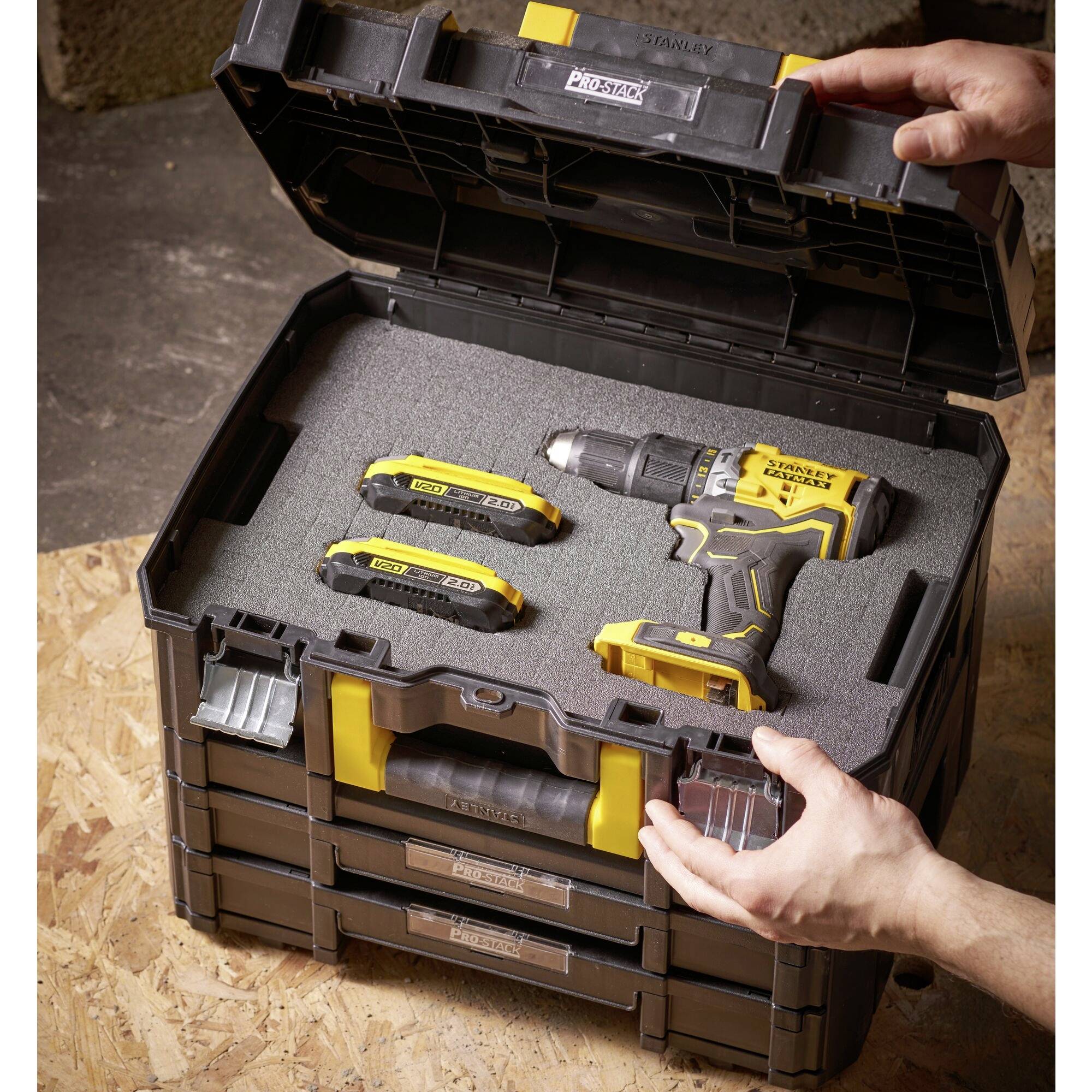 Un ensemble de perceuses-visseuses avec batteries dans un coffret à outils ouvert sur un sol en bois. Une personne tient le coffret.