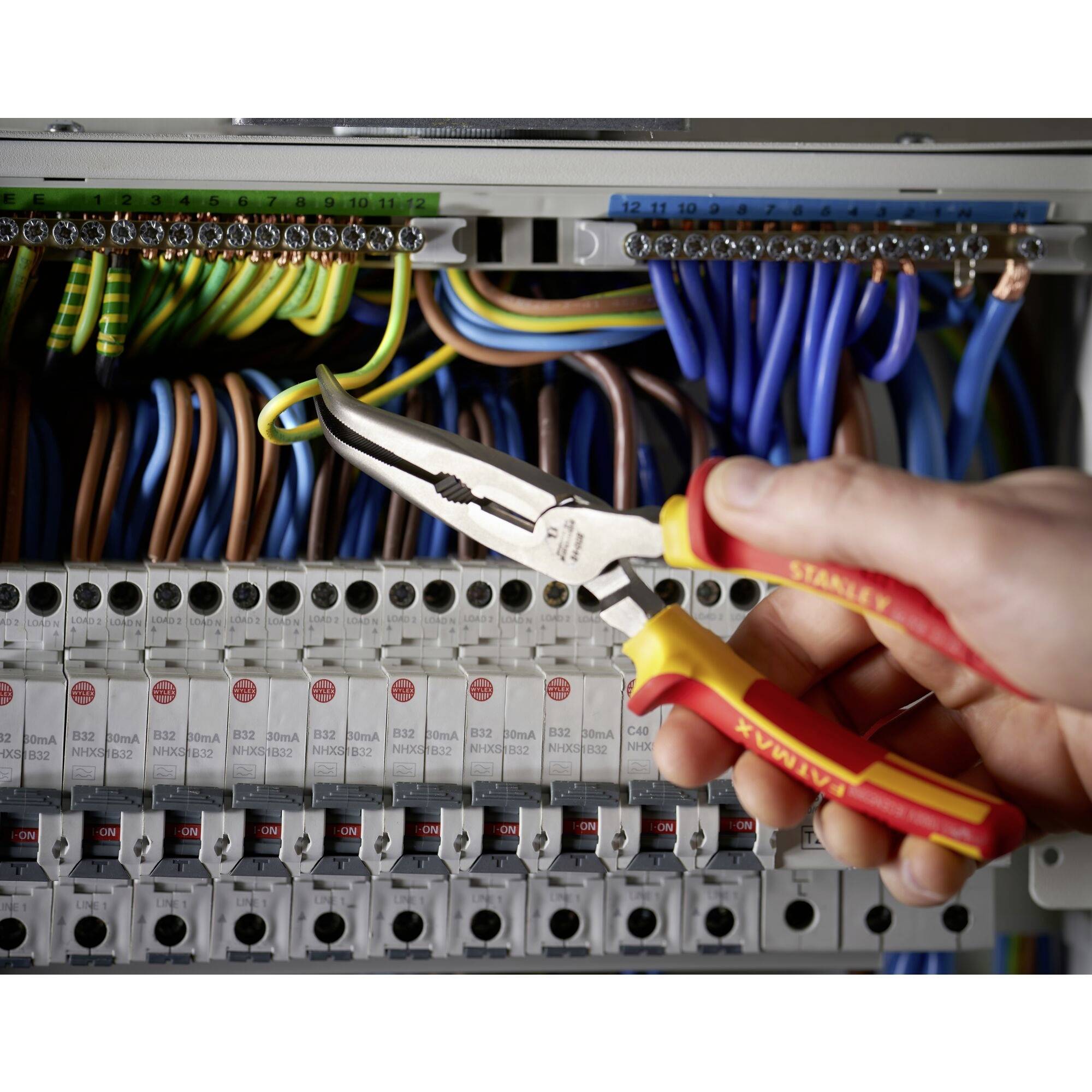 Une personne tient une pince isolée et travaille sur un coffret électrique ouvert comportant de nombreux câbles colorés.