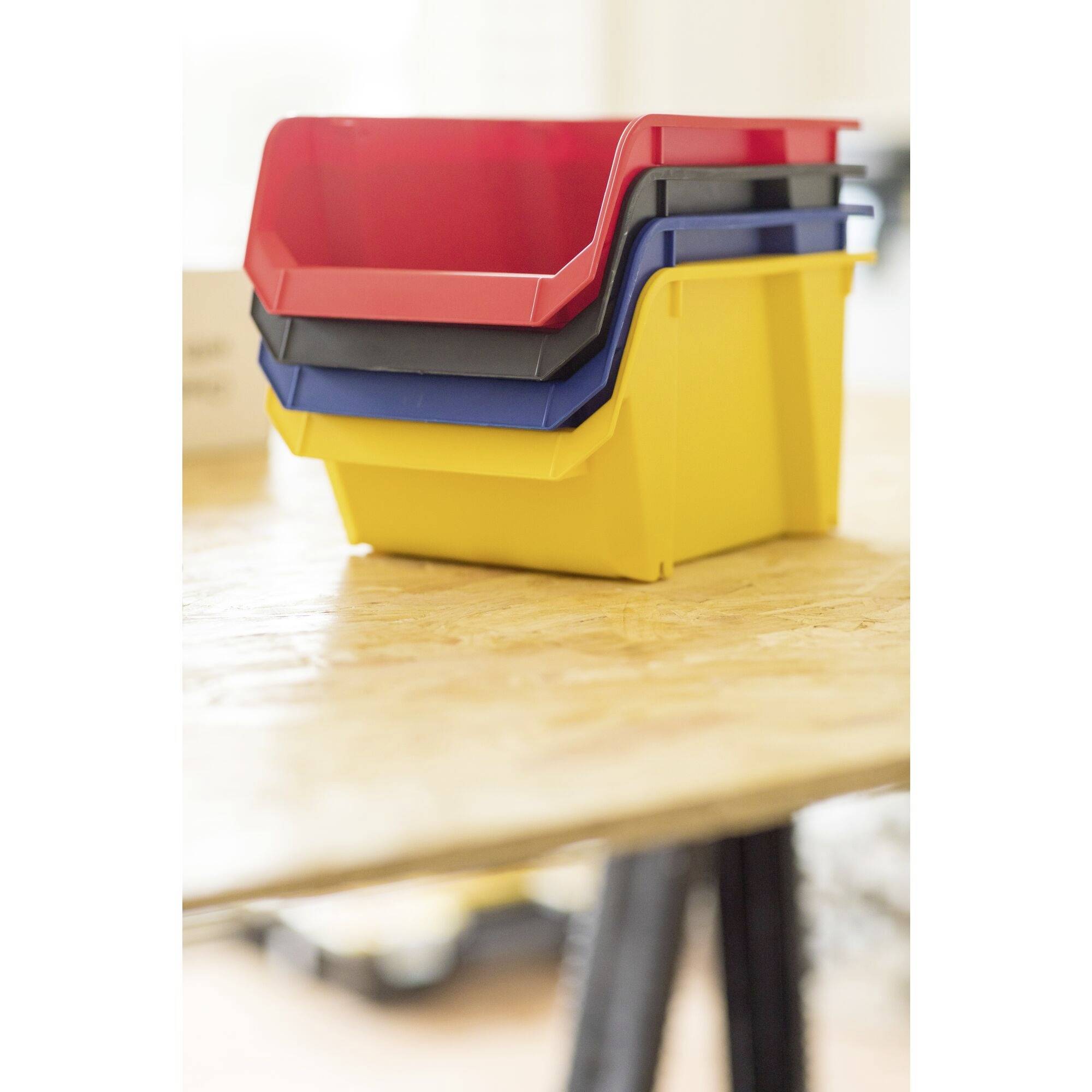 Quatre boîtes de rangement empilées en rouge, bleu, noir et jaune sont posées sur une table en bois.
