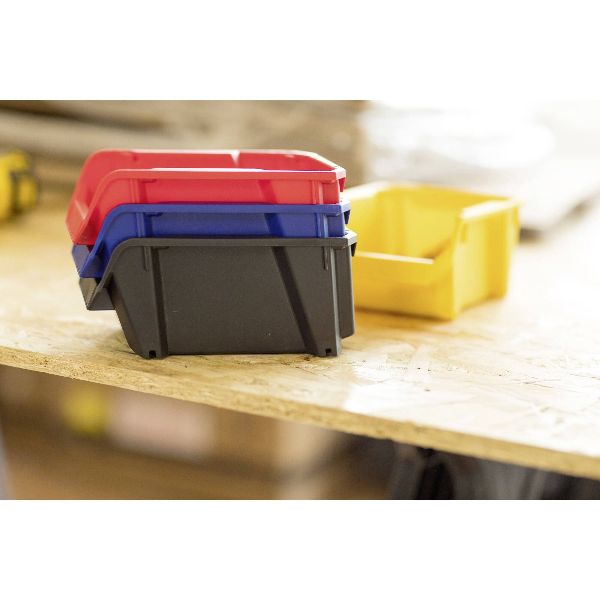 Trois boîtes de peinture empilées en rouge, bleu et noir sur une table en bois, avec une boîte jaune en arrière-plan. Environnement d'atelier.