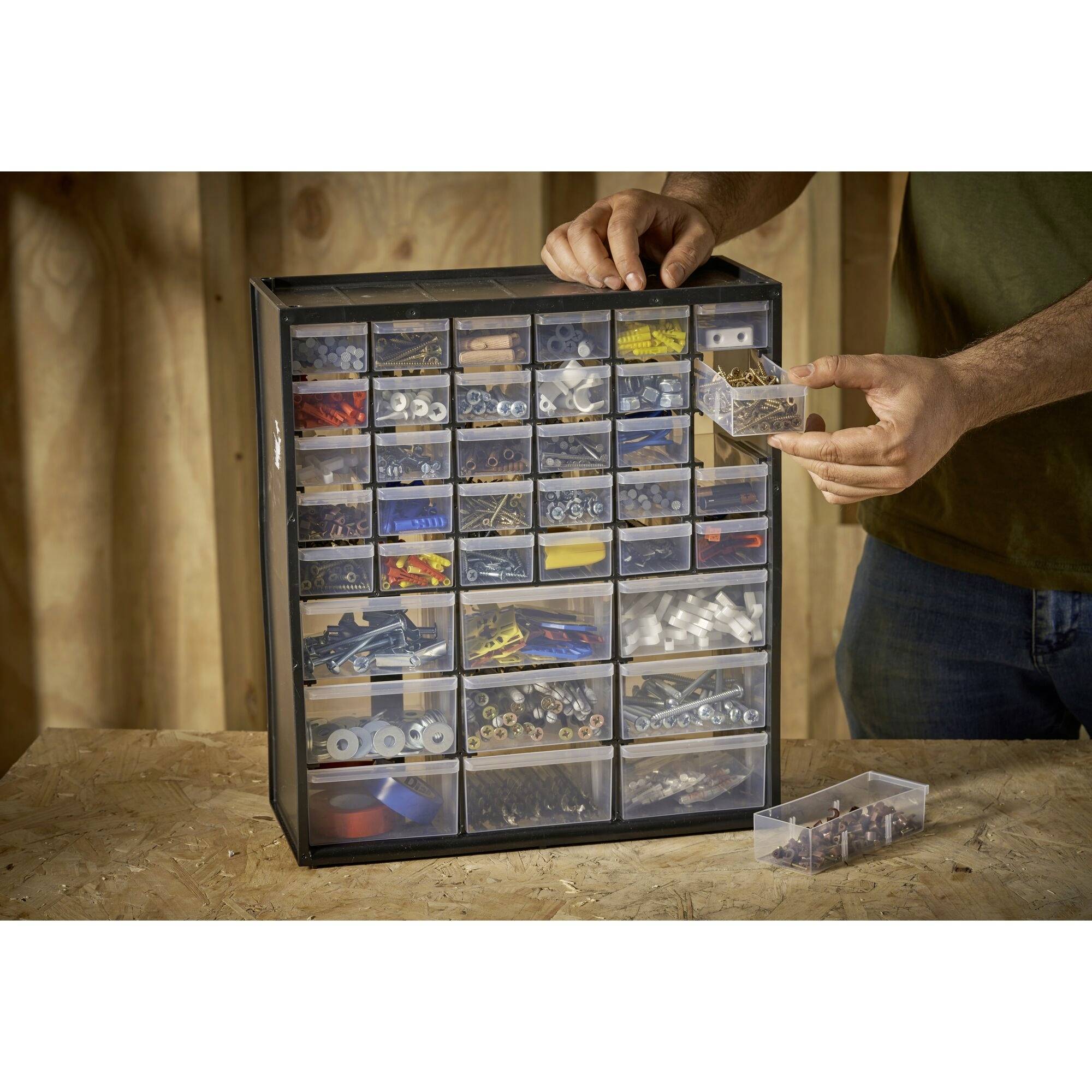 Une personne utilise un tiroir en plastique noir avec de nombreux compartiments pour organiser de petites pièces métalliques et en plastique.