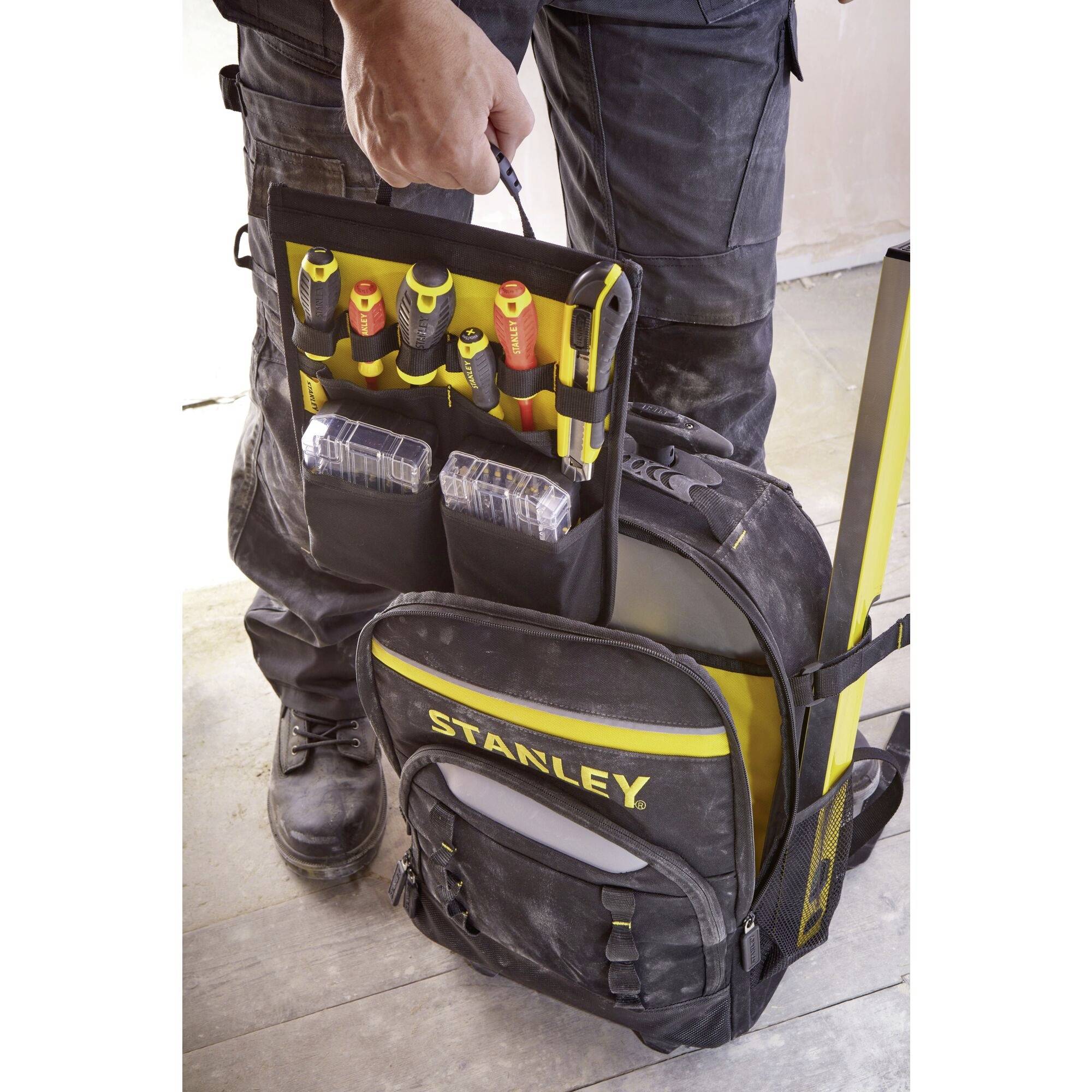 Une personne tient un sac à dos à outils avec plusieurs compartiments. Des tournevis et de petites boîtes sont visibles.