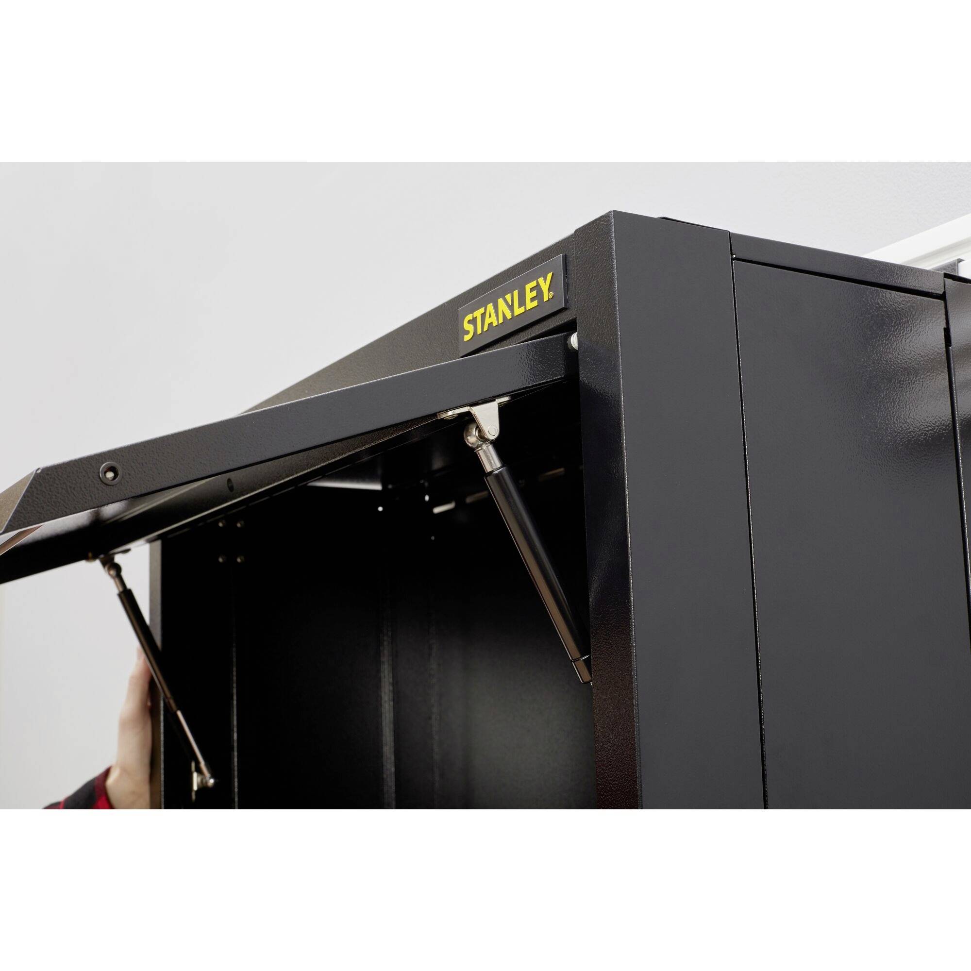 Un armoire métallique noire avec l'inscription jaune 'STANLEY' sur la porte, qui montre un mécanisme hydraulique pour l'ouverture.