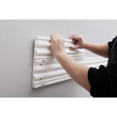 Une personne installe un panneau mural blanc sur un mur gris, en l'alignant soigneusement avec ses deux mains.