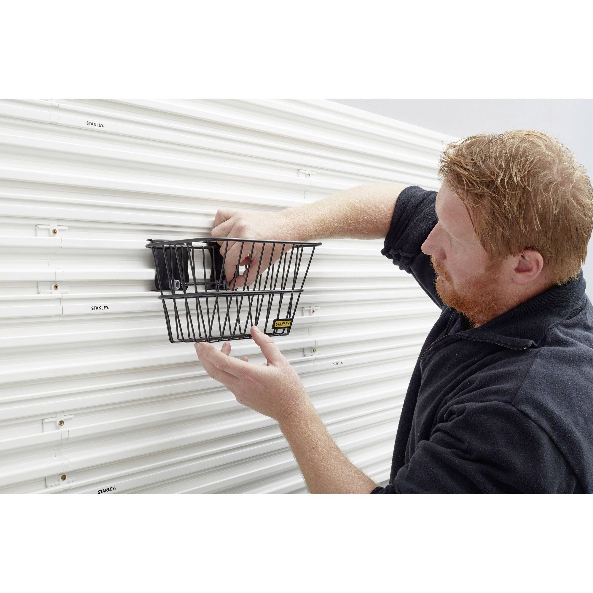Un homme fixe un panier noir sur un panneau blanc strié.