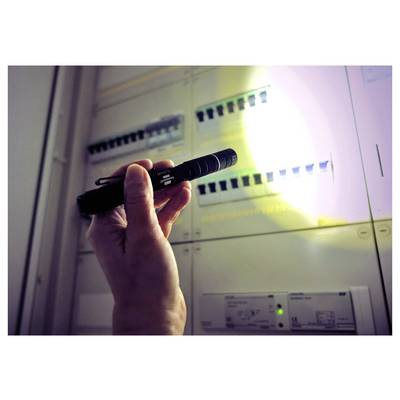 Une main tient une lampe de poche brillant sur un panneau électrique, illuminant les disjoncteurs et les étiquettes pour inspection.
