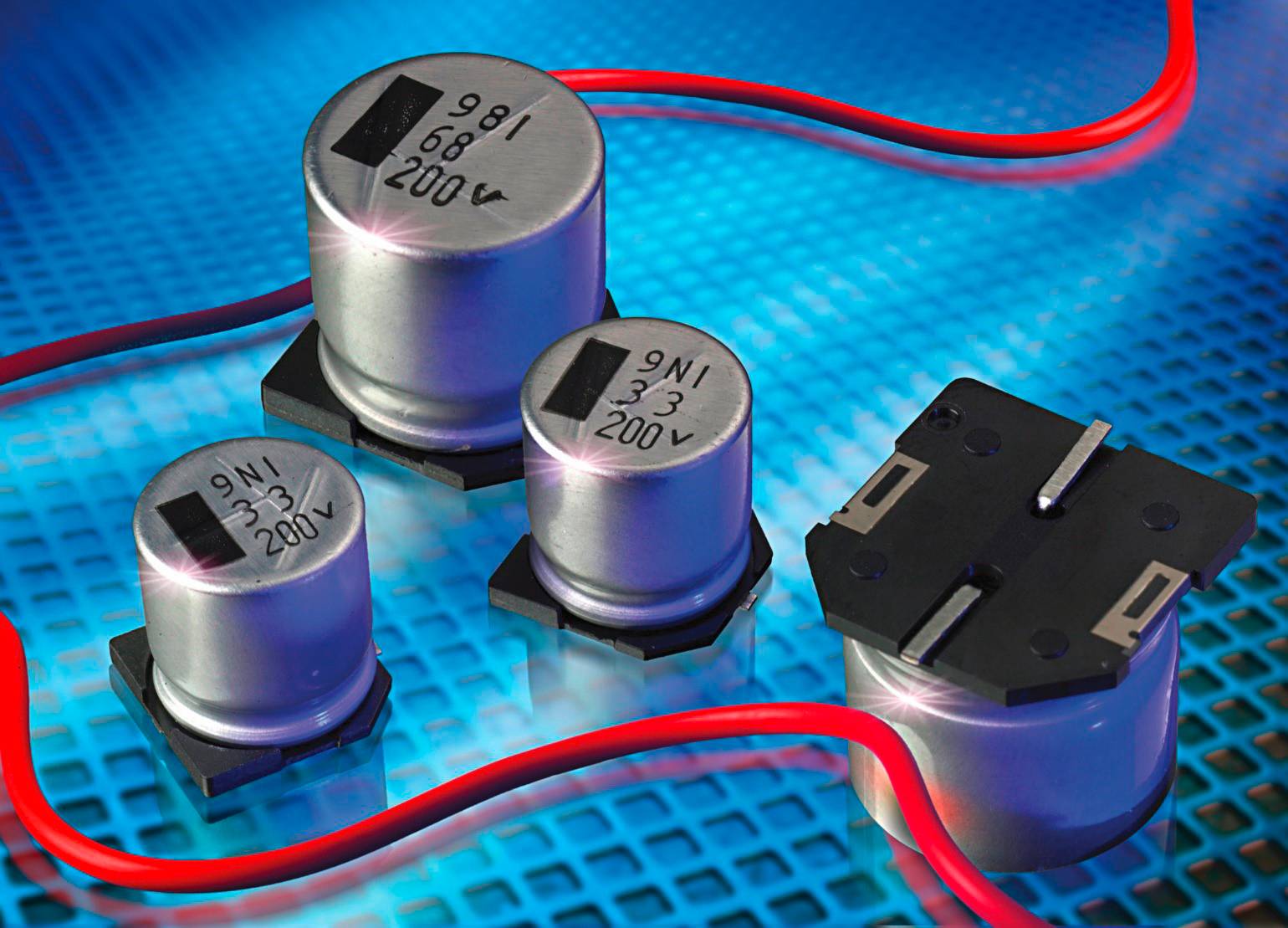 Quatre composants électriques cylindriques sur un fond métallique avec des câbles rouges. Chaque composant est étiqueté avec des valeurs de tension.