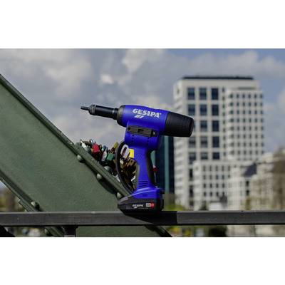 Un tournevis sans fil bleu portant l'inscription 'GESIPA' est posé sur un support métallique. Des bâtiments flous sont visibles en arrière-plan.