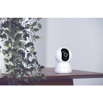 Caméra de surveillance posée sur une table à côté d'une plante. La caméra est sphérique et moderne, installée sur un socle blanc.