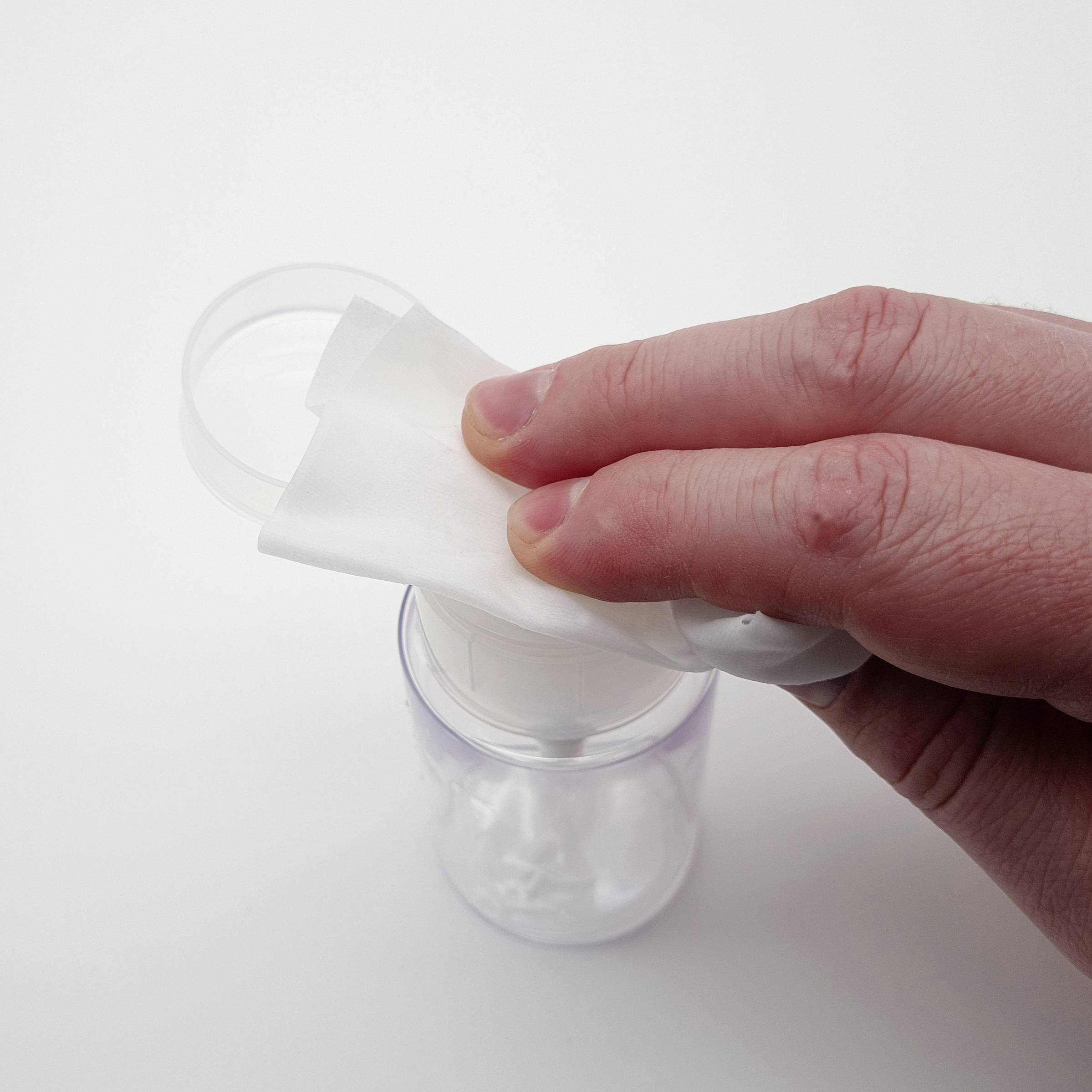 Une main appuie une compresse de coton sur un distributeur de savon.