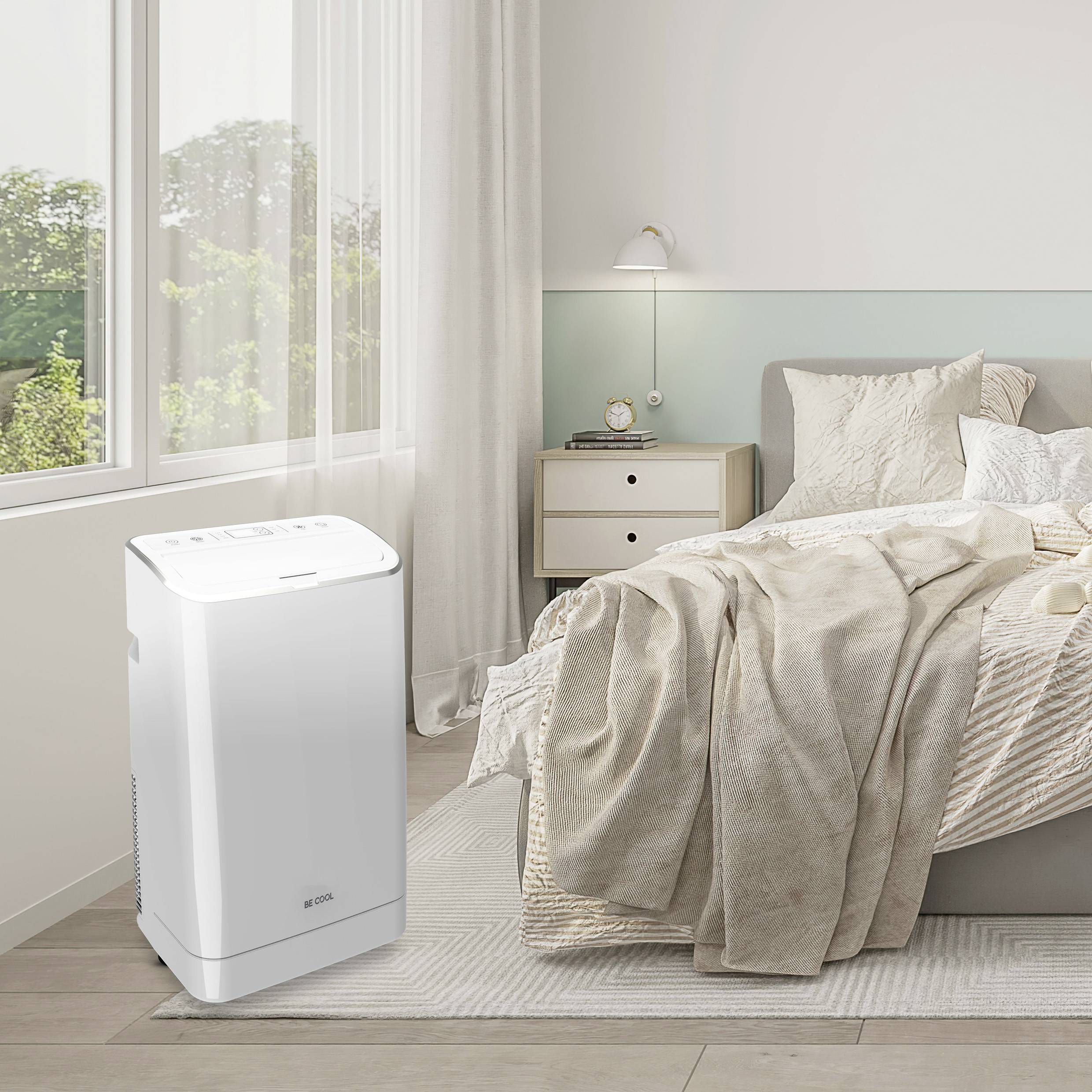 Une chambre à coucher avec un purificateur d'air moderne à côté d'un lit confortable. De grandes fenêtres laissent entrer la lumière du jour dans la pièce.