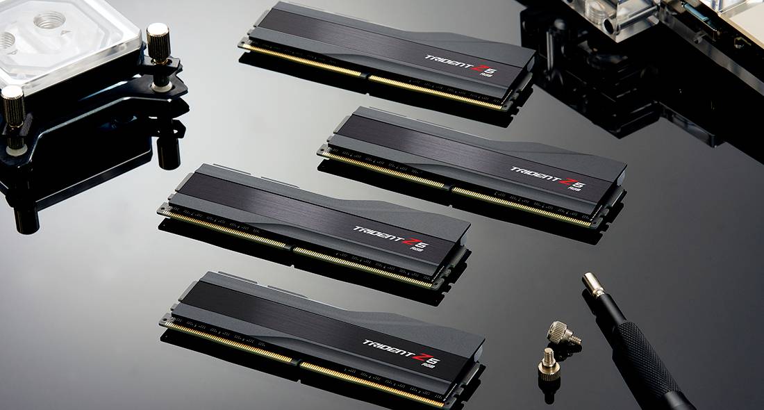Quatre modules RAM noirs reposent sur une surface brillante, entourés de vis et d'un tournevis.