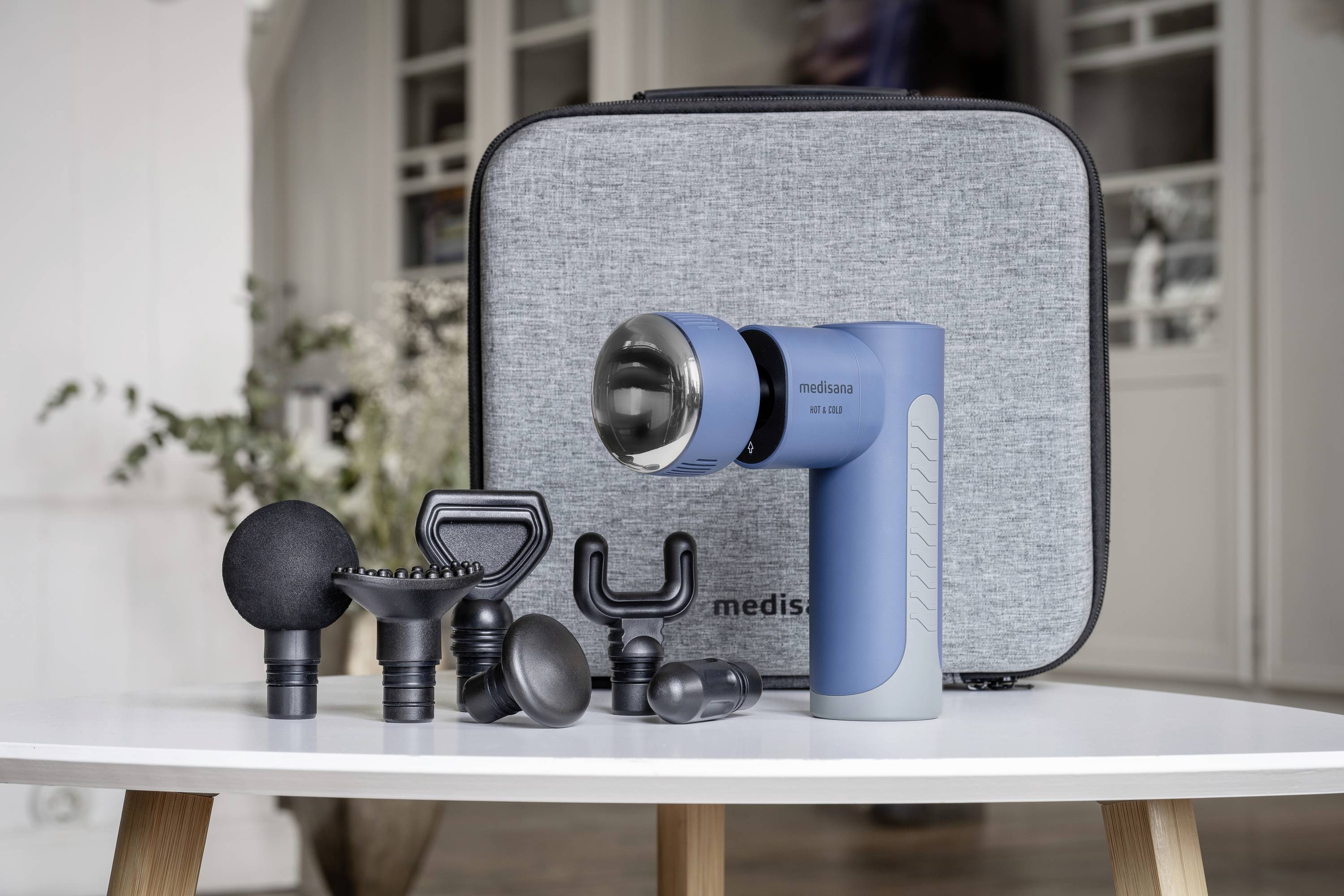 Pistolet de massage avec différents embouts posé sur une table, sac en arrière-plan. Adapté pour la détente musculaire et la récupération.