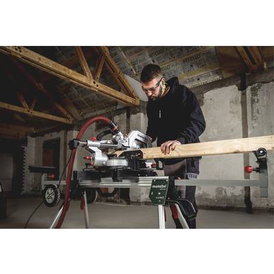 Un homme travaille avec concentration à l'aide d'une scie à onglets électrique dans un grand hall en construction.