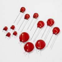 Des condensateurs céramiques rouges de différentes tailles avec des fils disposés sur une surface grise.