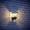 Lampe extérieure éclairée contre un mur de briques dans l'obscurité, créant une lueur chaleureuse sur le mur.