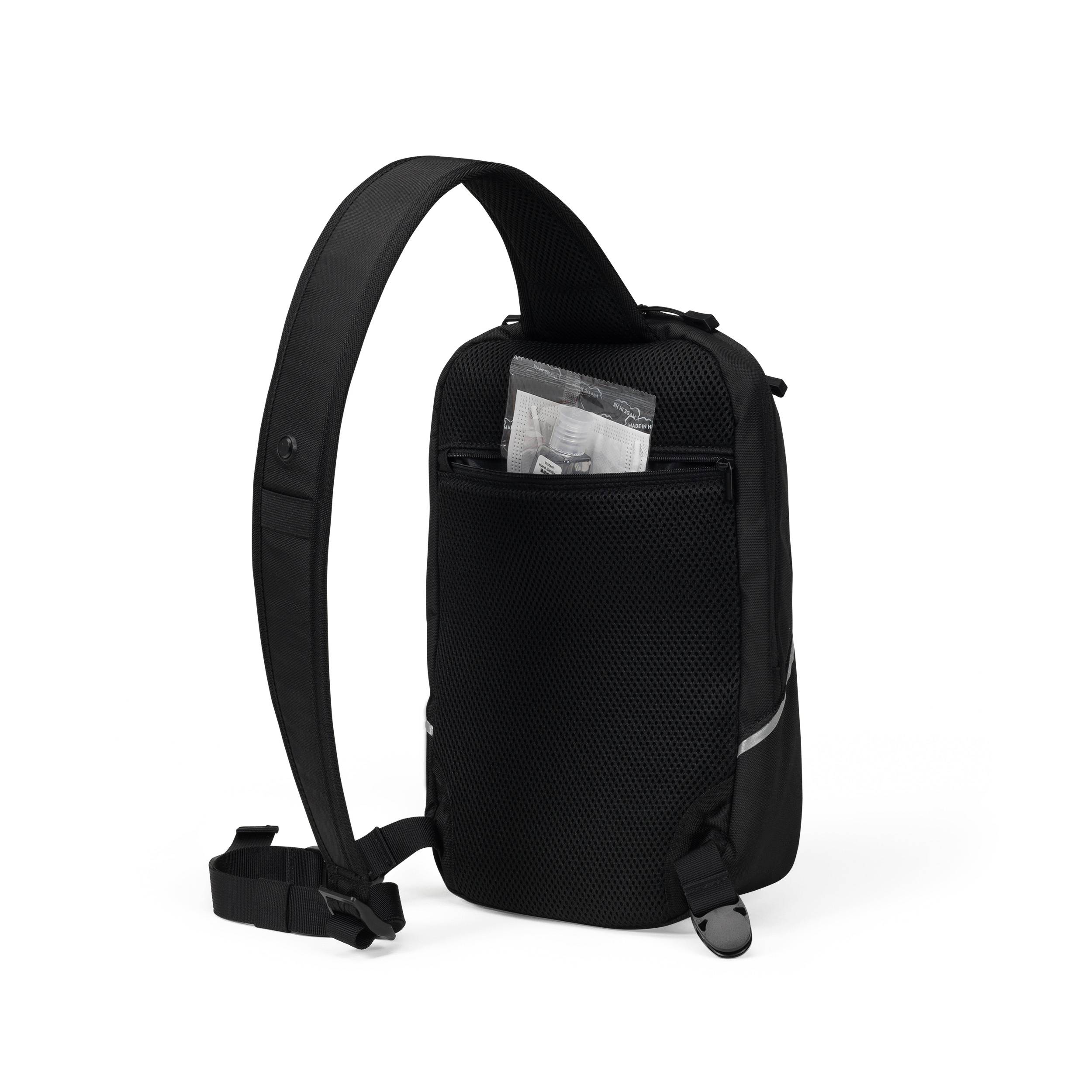 Un sac à bandoulière noir avec une seule bretelle. Il possède une poche avant en filet avec un papier visible à l'intérieur.