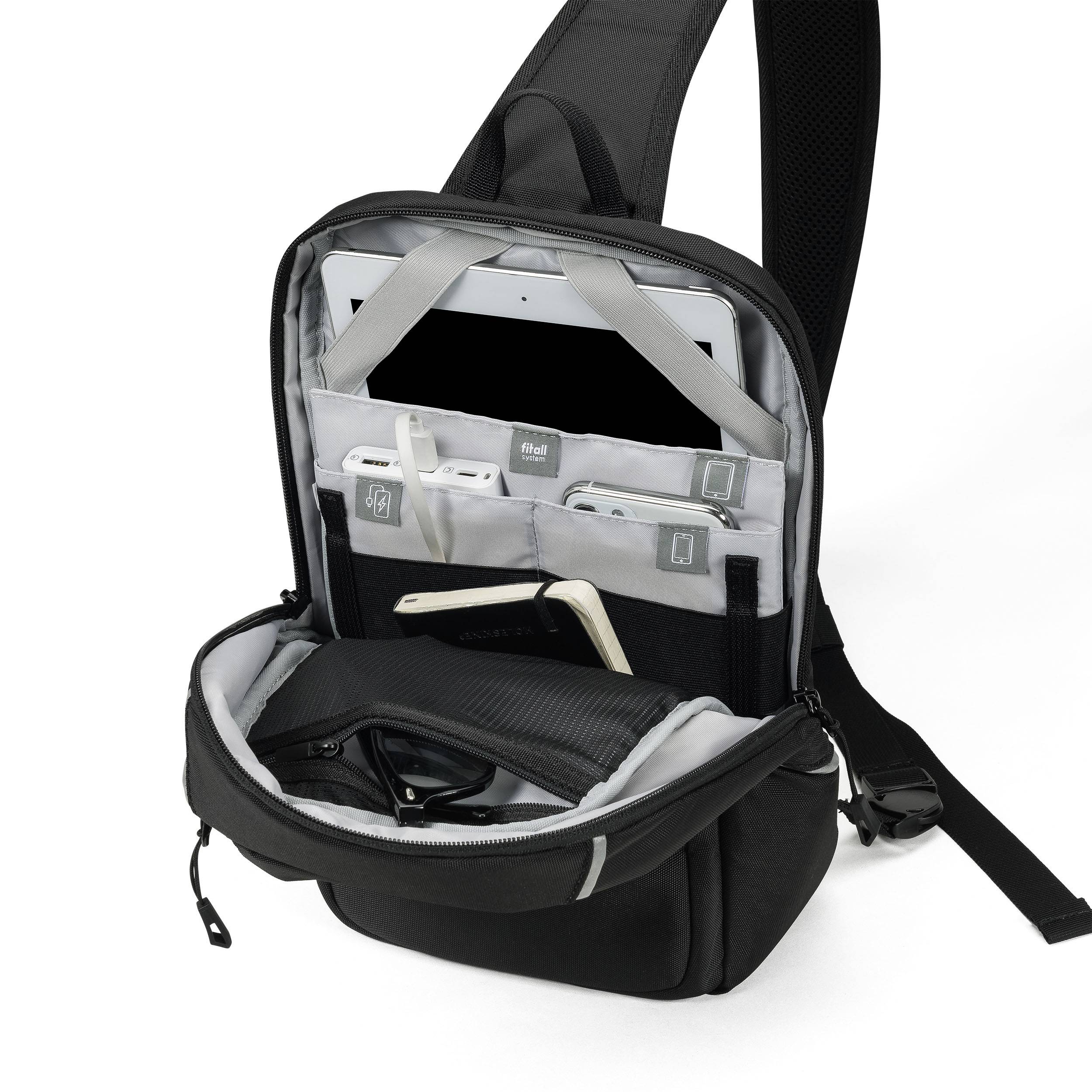 Sac à bandoulière noir ouvert avec plusieurs compartiments. À l'intérieur se trouvent une tablette, un carnet et plusieurs câbles rangés dans des élastiques.