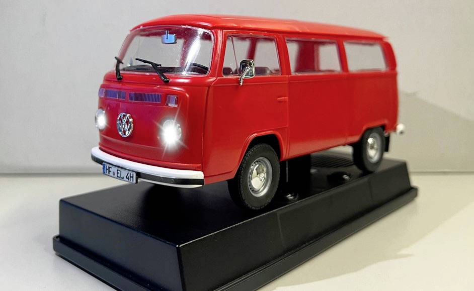Voiture miniature rouge d'un van Volkswagen classique, présentée sur un socle noir.