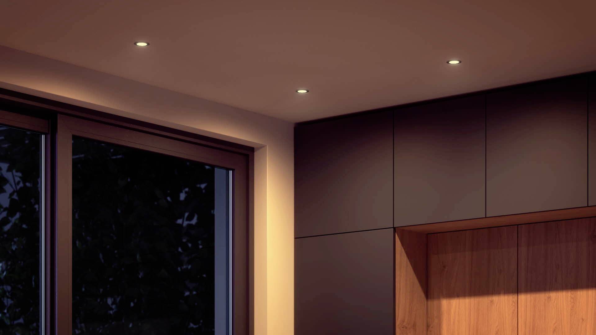 Aménagement intérieur moderne avec des murs en bois foncé et de grandes fenêtres offrant une vue nocturne. Des spots de plafond discrets éclairent la pièce.