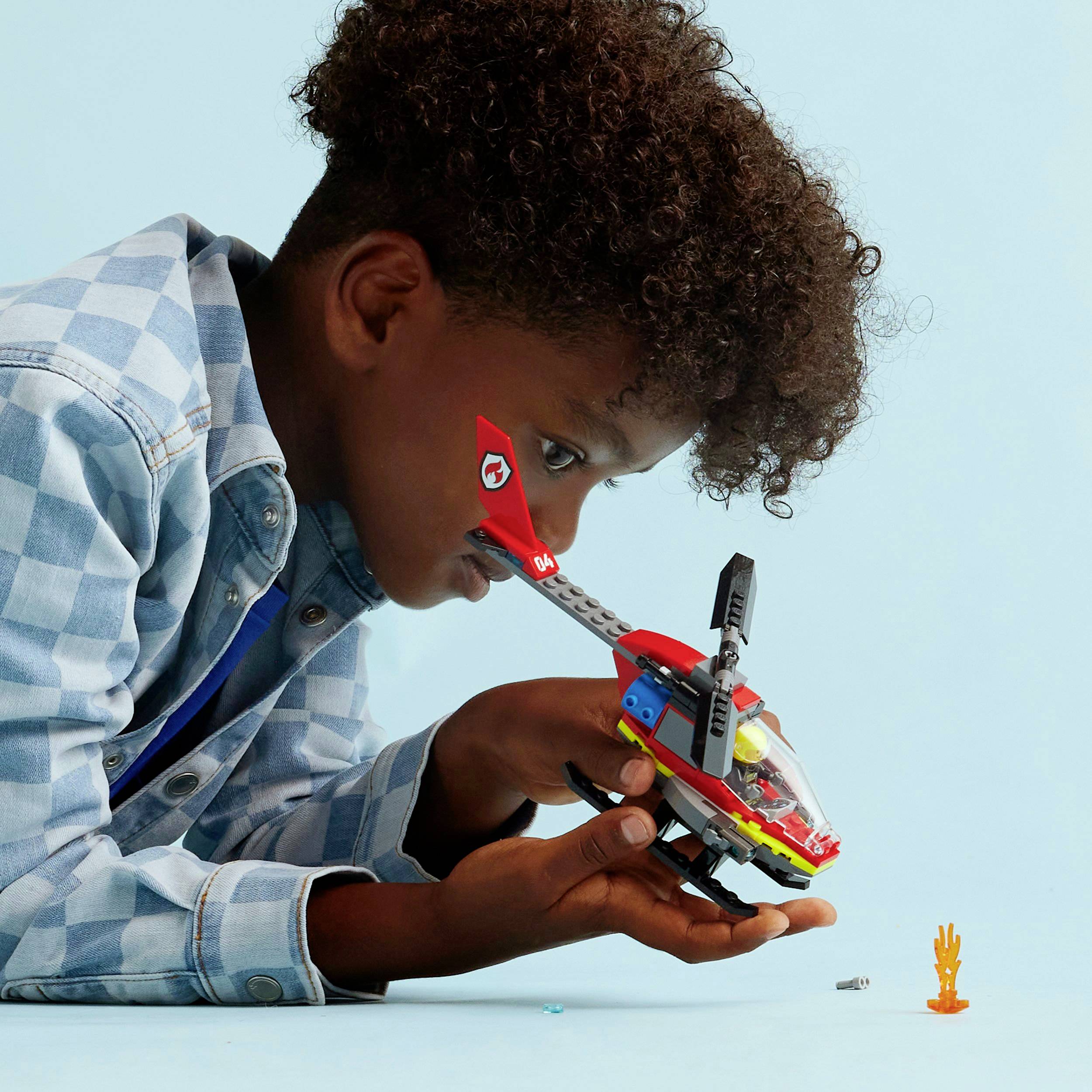 Un enfant joue de manière concentrée avec un hélicoptère jouet devant un fond bleu.