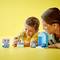 Un enfant sourit et joue avec des blocs de construction colorés, tandis qu'un adulte est assis à côté et regarde. Fond jaune.