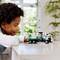 Un enfant joue avec un petit camion-jouet sur le thème du recyclage, posé sur une table. Des plantes vertes sont visibles en arrière-plan.