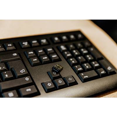 Un clavier d'ordinateur noir avec un petit dongle USB posé sur les touches.