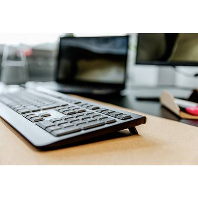 Bureau avec un écran d'ordinateur flou en arrière-plan, un clavier noir moderne au premier plan, illustrant un environnement de travail.