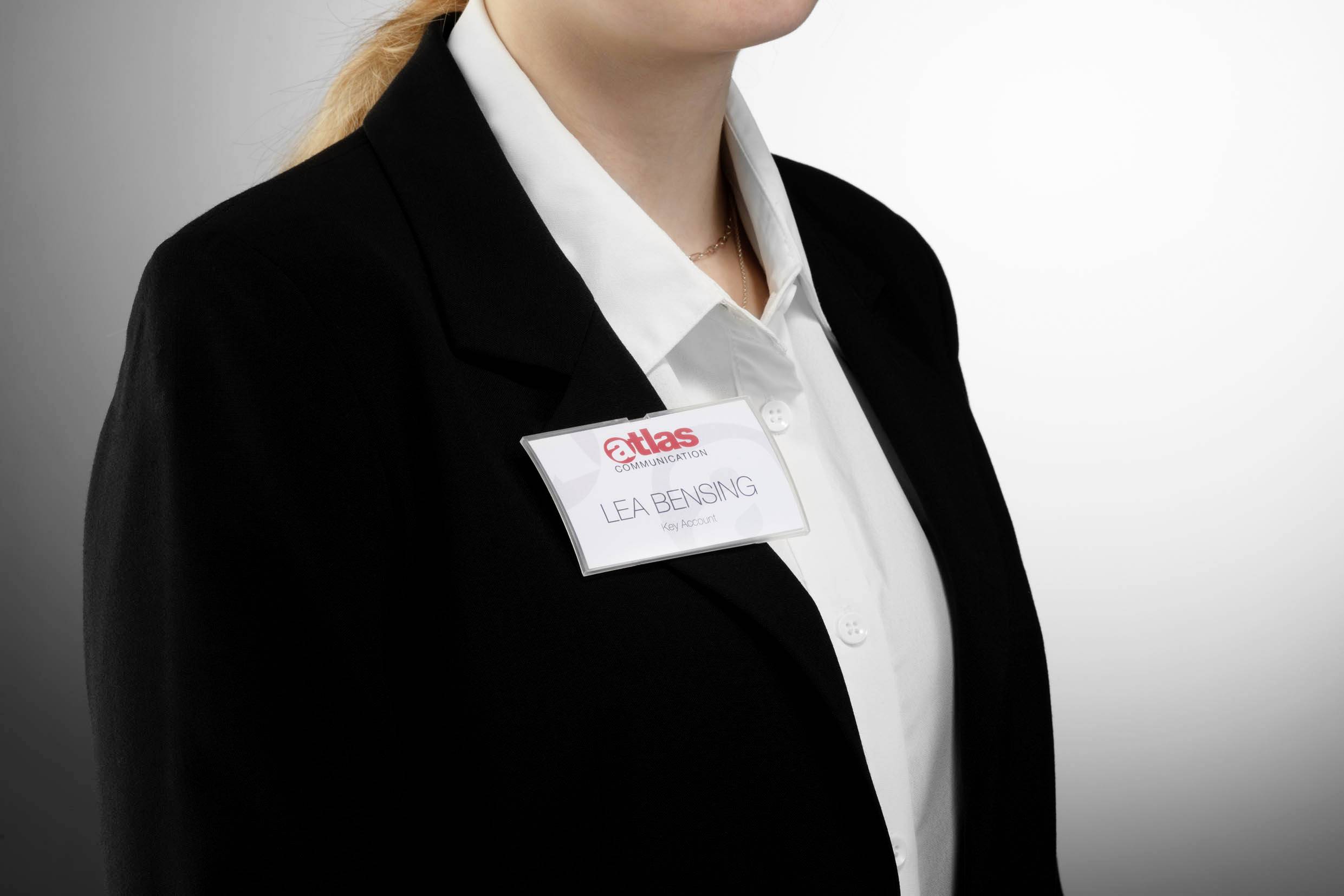 Une personne portant un costume noir porte un badge sur lequel est inscrit 'Lea Bensing'.