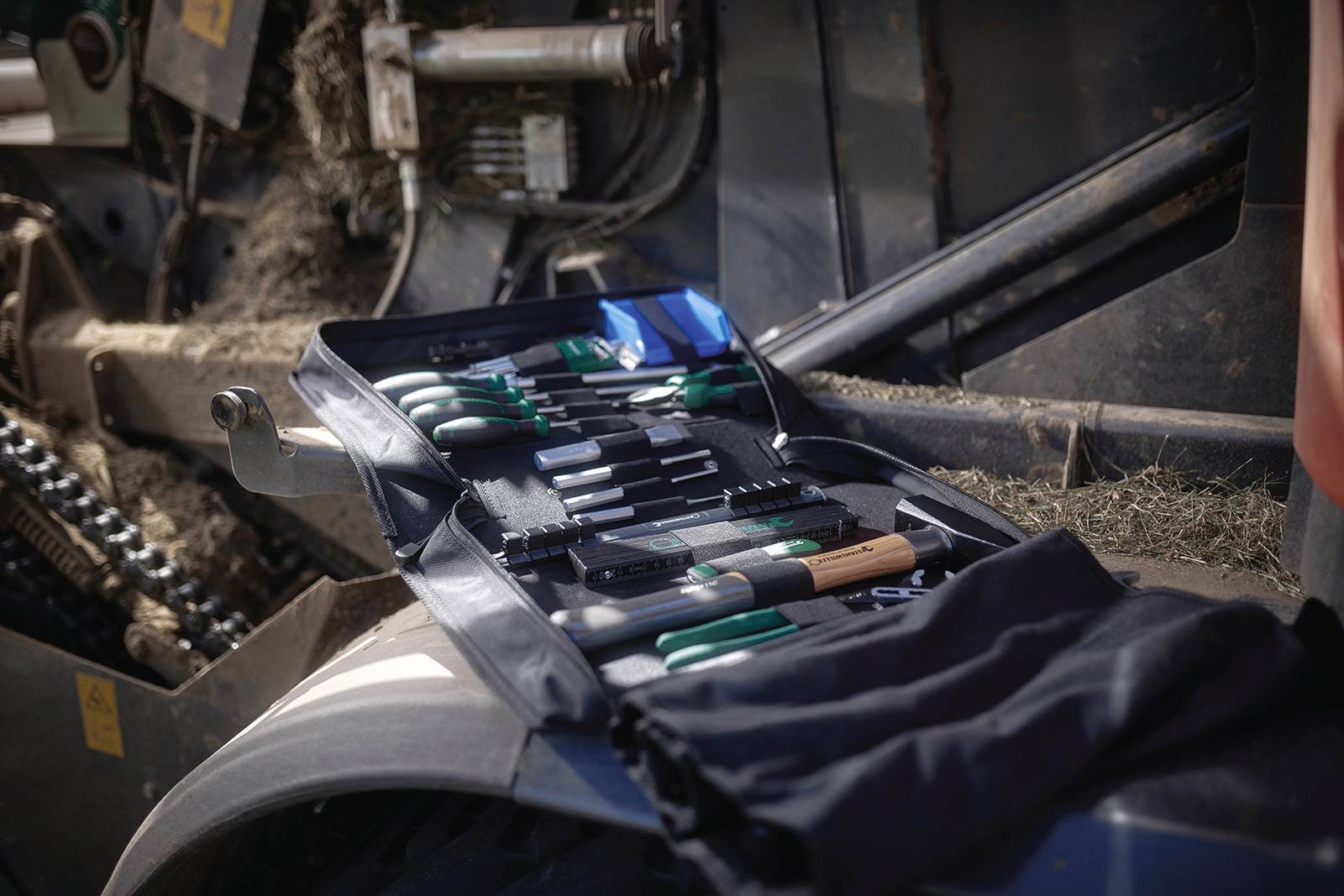 Ensemble d'outils comprenant différentes pinces et tournevis posé sur une machine agricole. Des pièces mécaniques sont visibles en arrière-plan.