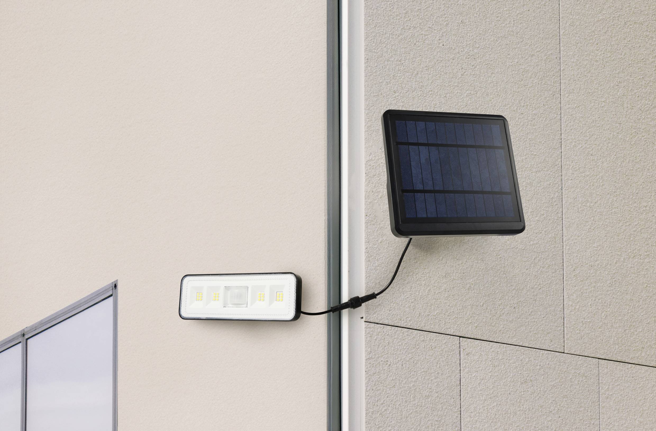 Lampe solaire fixée à un mur extérieur, reliée à un panneau solaire. La lampe est adaptée à l'éclairage extérieur économe en énergie.